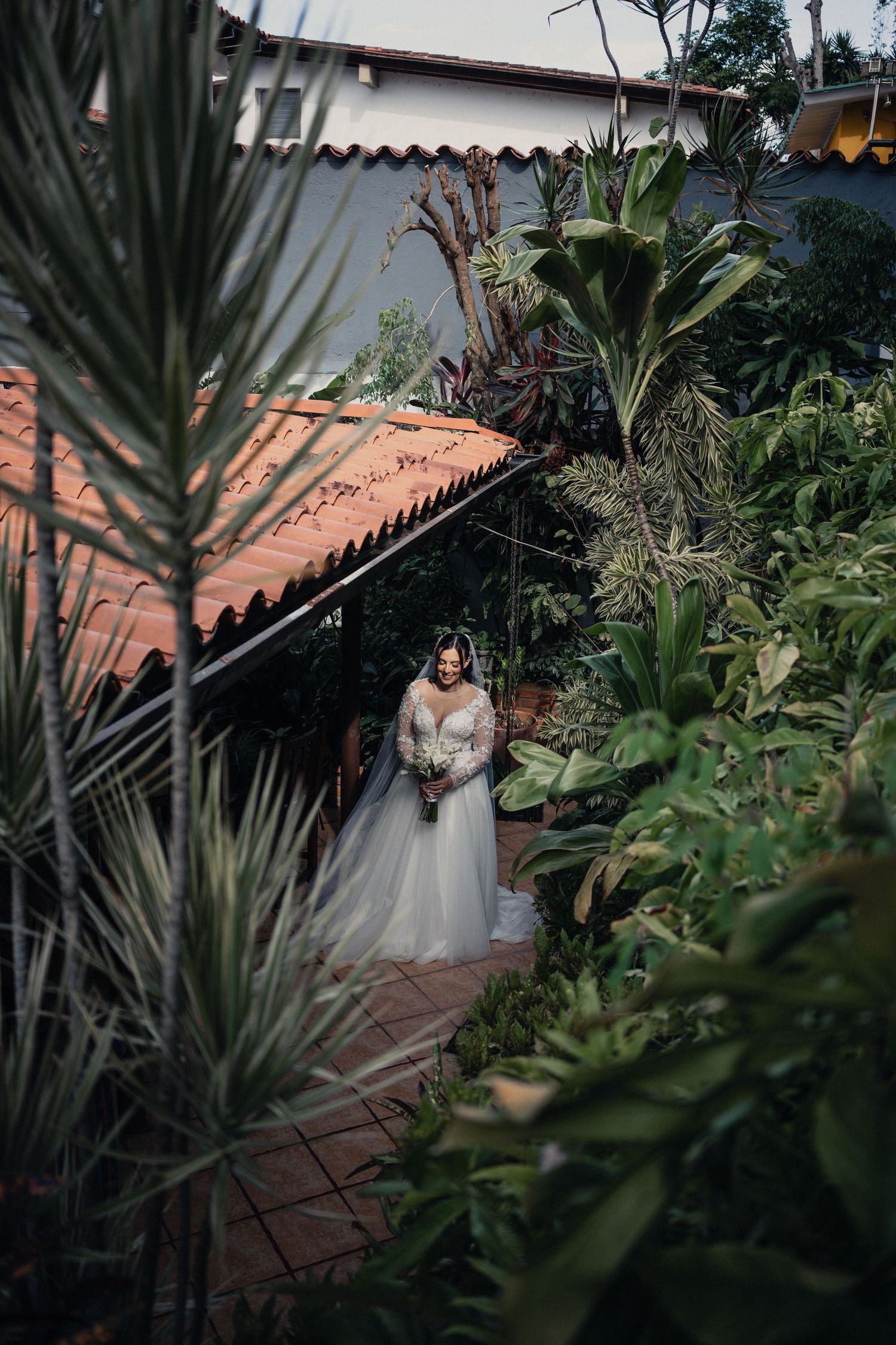 Lush tropical garden pathway with terracotta tile roof and palm fronds creating a romantic wedding setting.