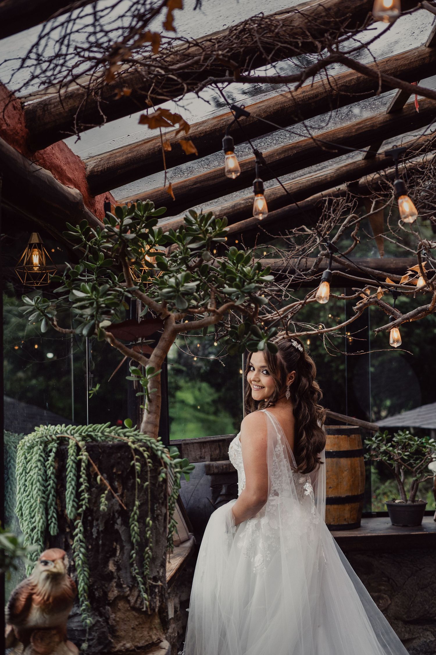 A bridal gown is displayed in a charming outdoor setting with twinkle lights and wooden beams overhead.