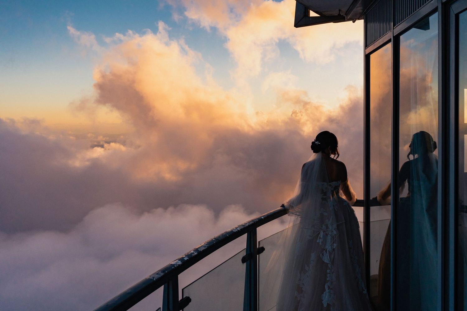 Silhouettes of people standing on an observation deck against a dramatic sunset sky with pink and orange clouds.