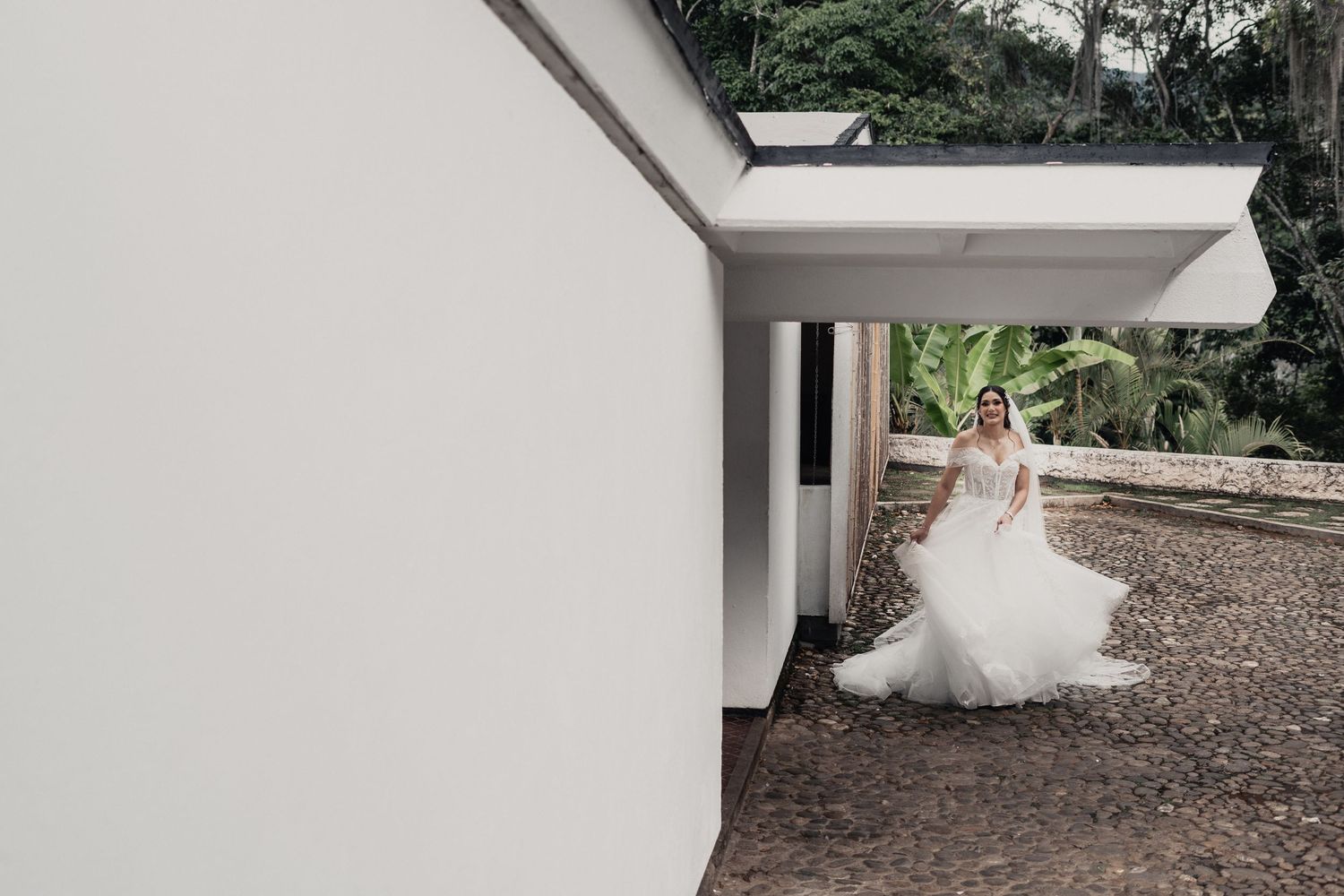A bride in a white ball gown twirls gracefully in front of a white wall and gravel pathway.
