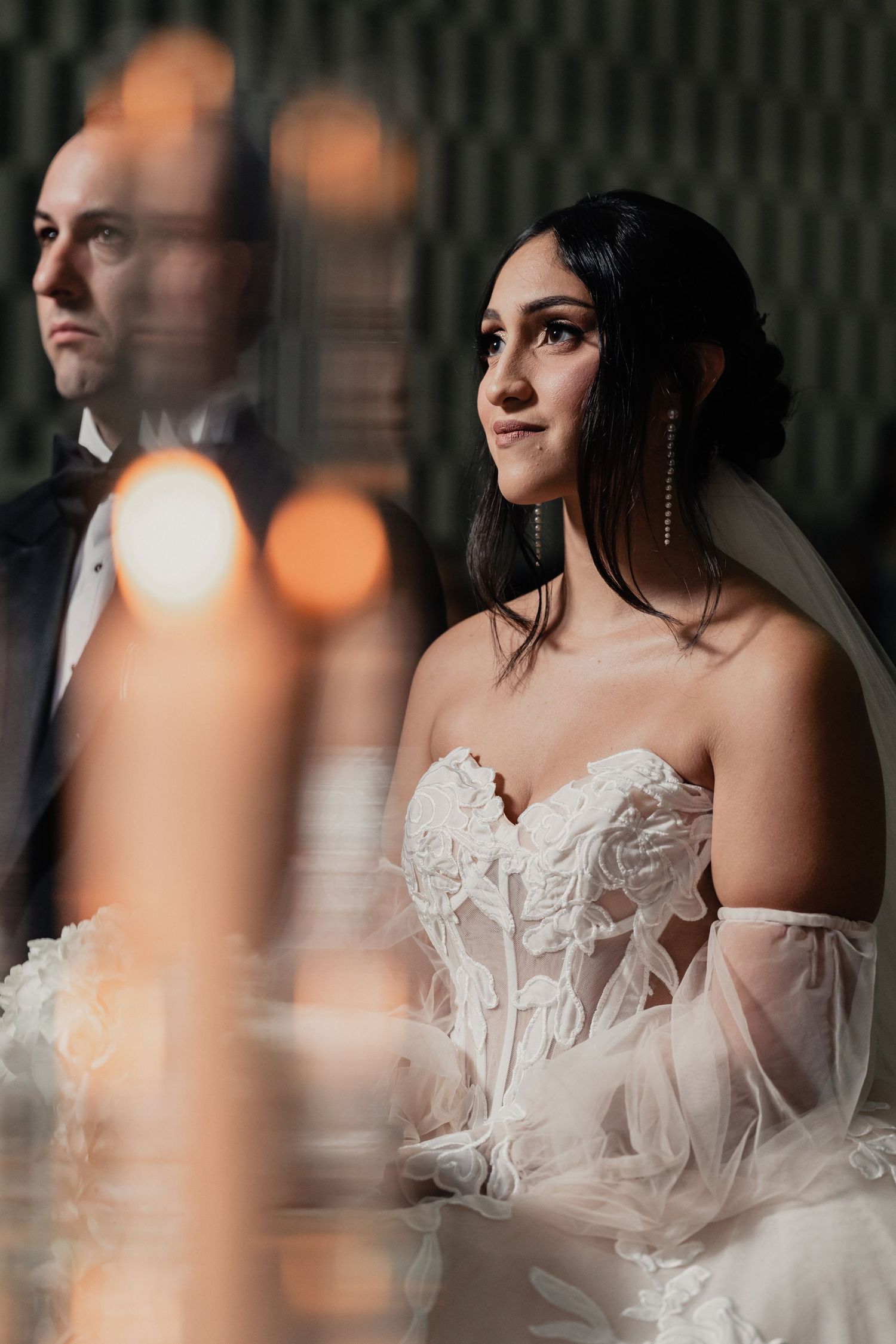 A bride in an elegant white strapless gown poses during her wedding celebration with soft bokeh lights.