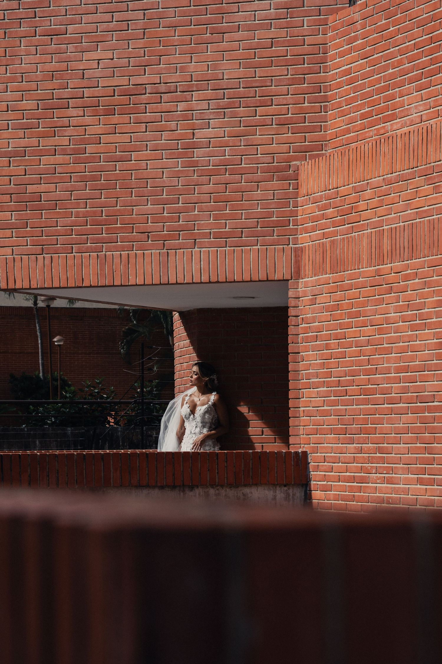 A minimalist wedding photo against red brick walls with dramatic shadows and lighting.