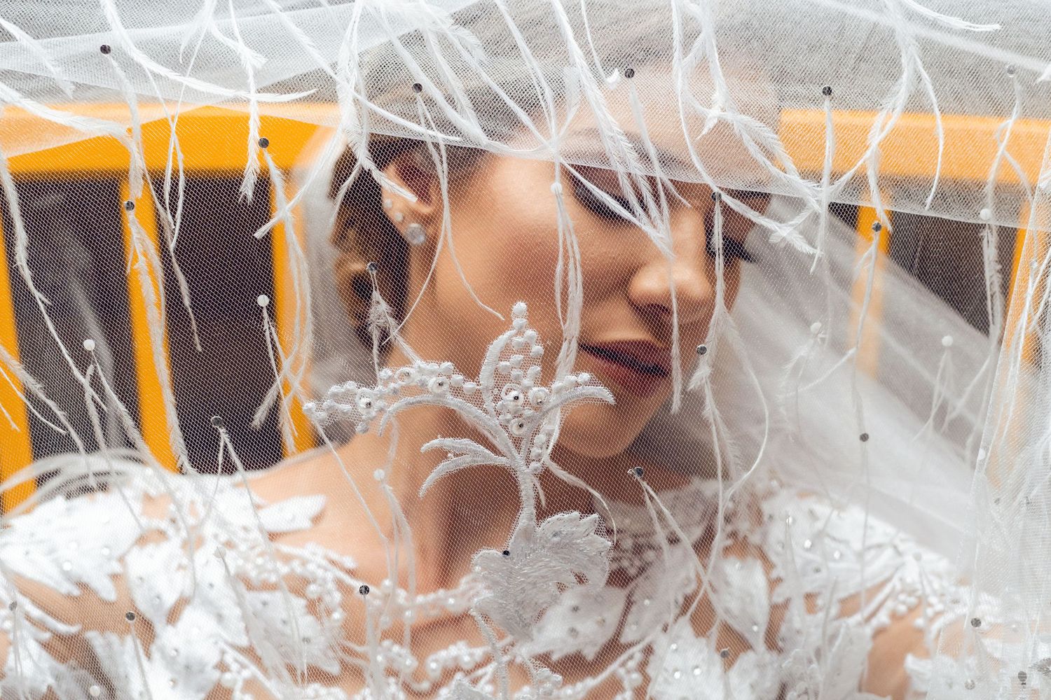 A person wearing a white wedding dress is surrounded by delicate lace veils and fabric in a soft, ethereal setting.
