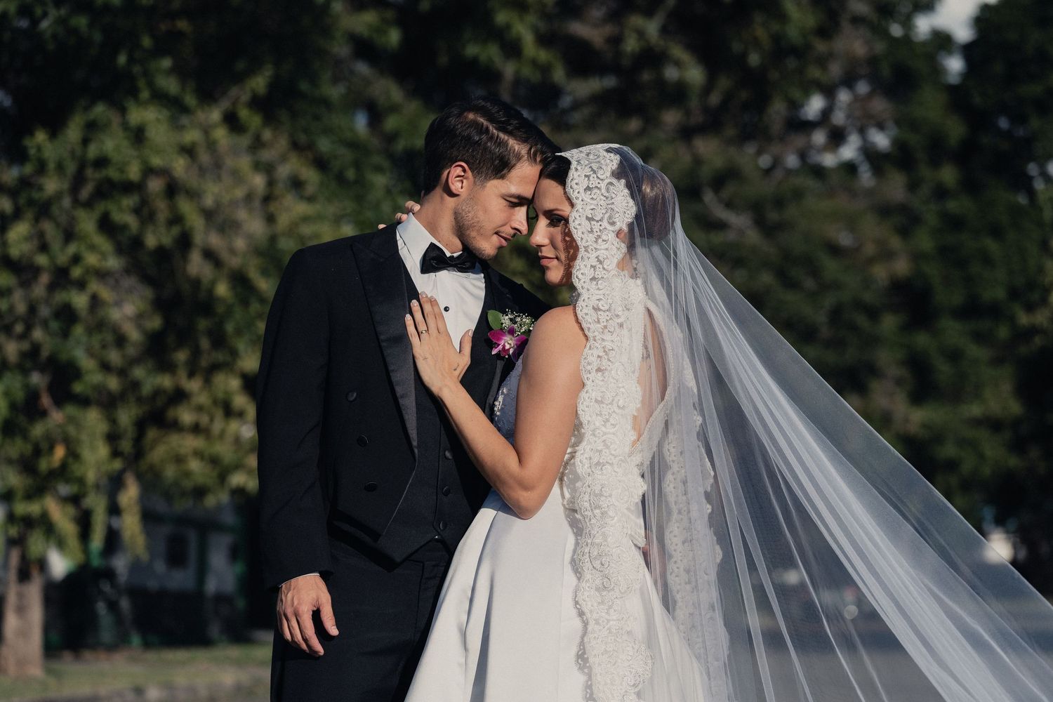Elegant outdoor wedding portrait with lush greenery and flowing white veil.