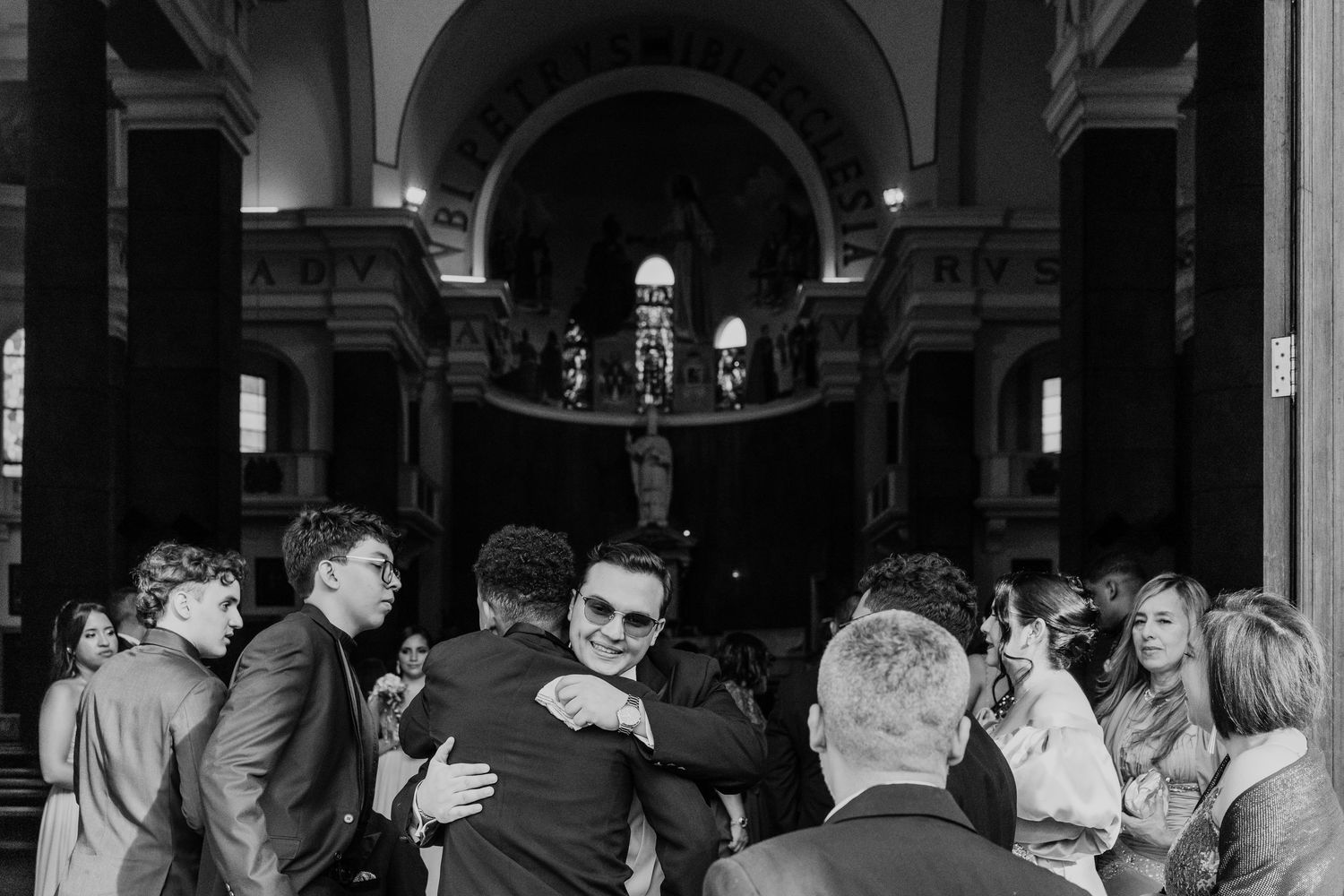 A black and white photograph shows a crowded reception or party scene with people mingling in an elegant indoor venue.