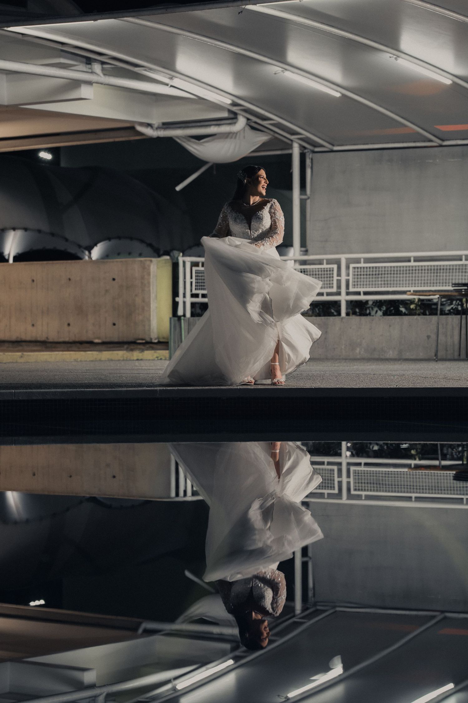 A person in white flowing fabric performs an artistic dance movement in an industrial parking garage space.