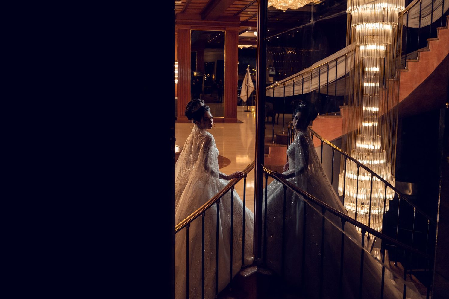 A silhouetted couple dances romantically on a staircase illuminated by warm glowing chandeliers.