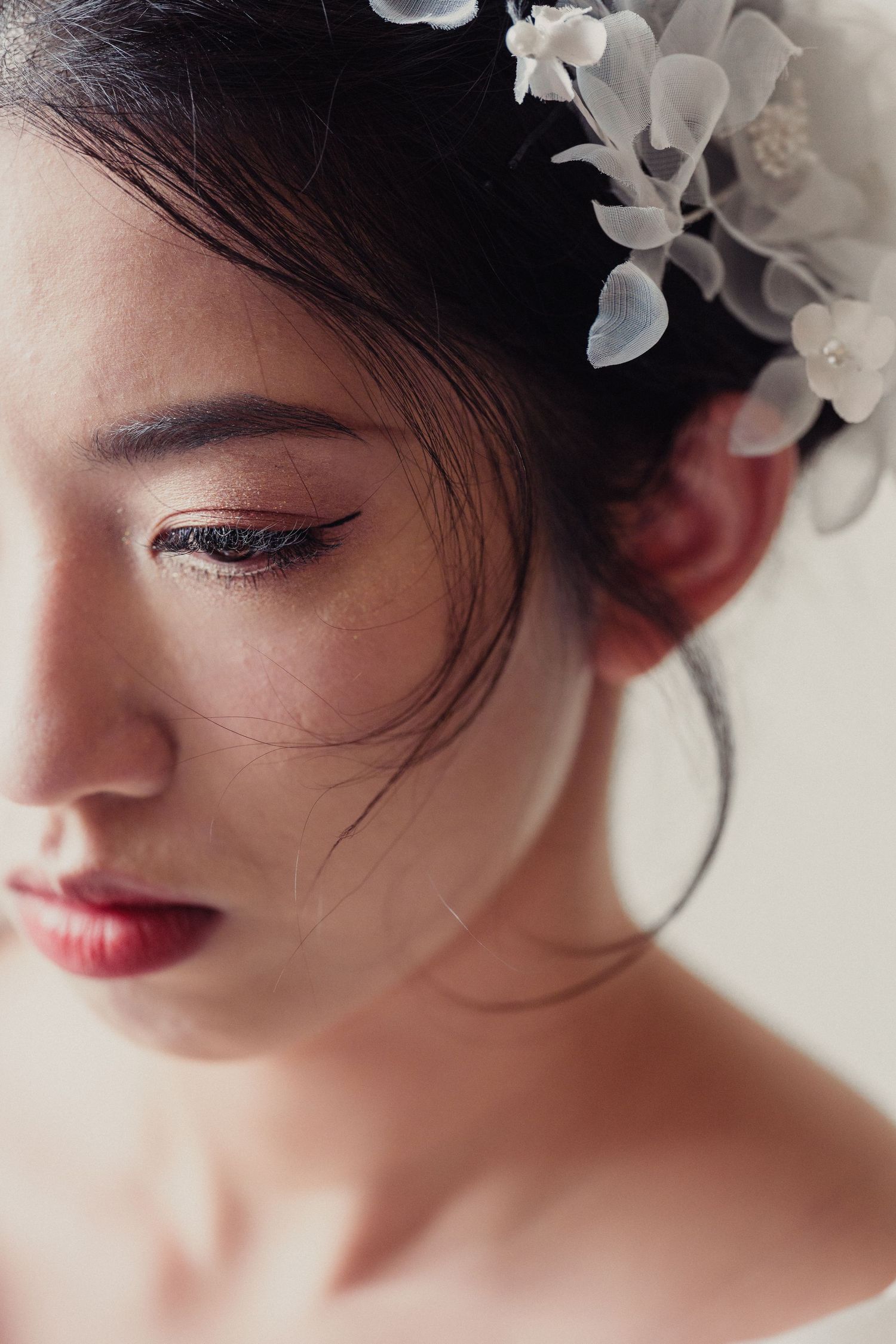 Close up beauty portrait with delicate white floral hair accessories and elegant makeup in soft lighting.