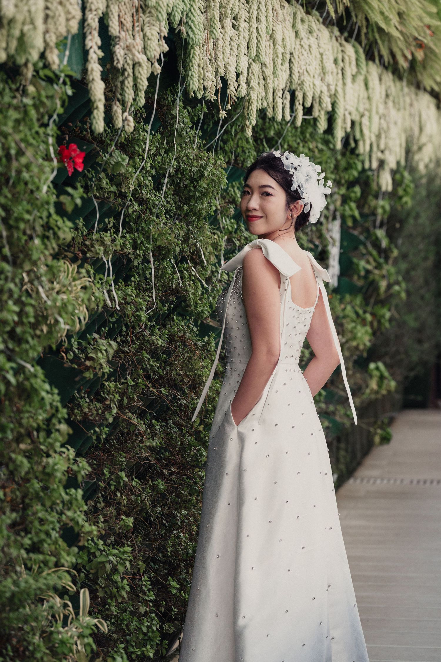 A white flower girl dress with delicate pearl details and lace accents shown from different angles in a garden setting.