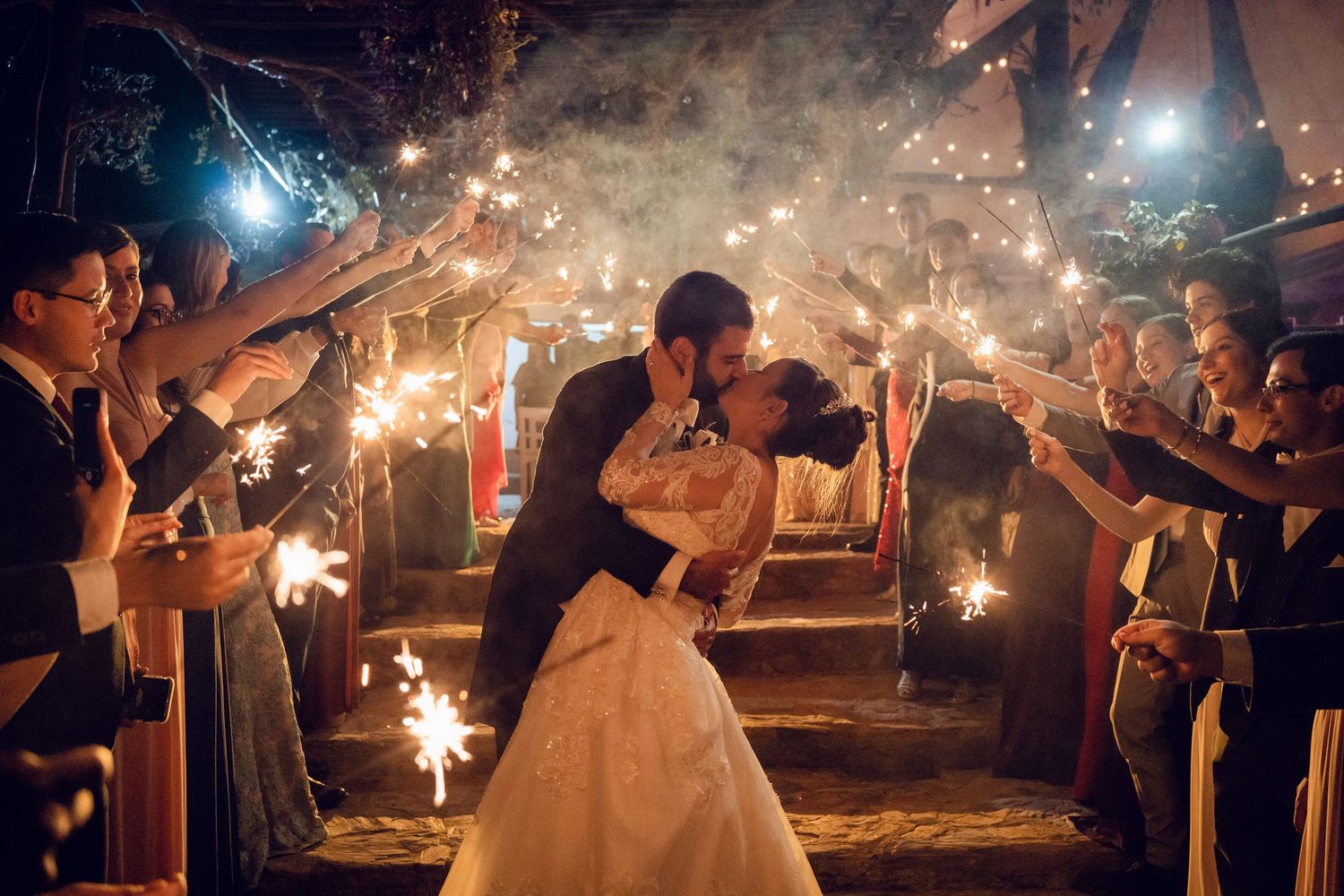 Guests hold sparklers creating a magical tunnel of light during a nighttime wedding celebration.