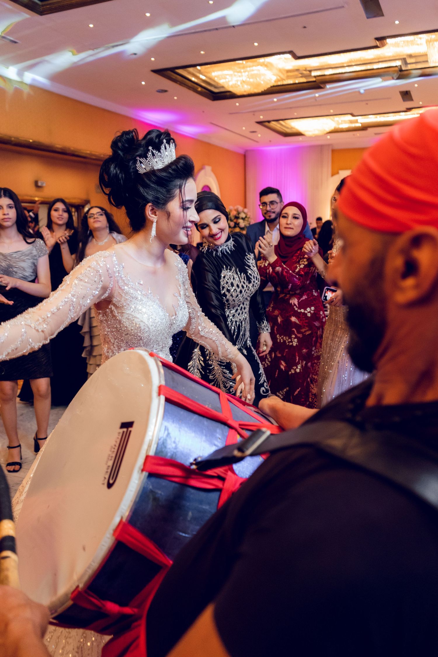 Wedding guests dance and celebrate at a lively indoor reception with colorful lighting.