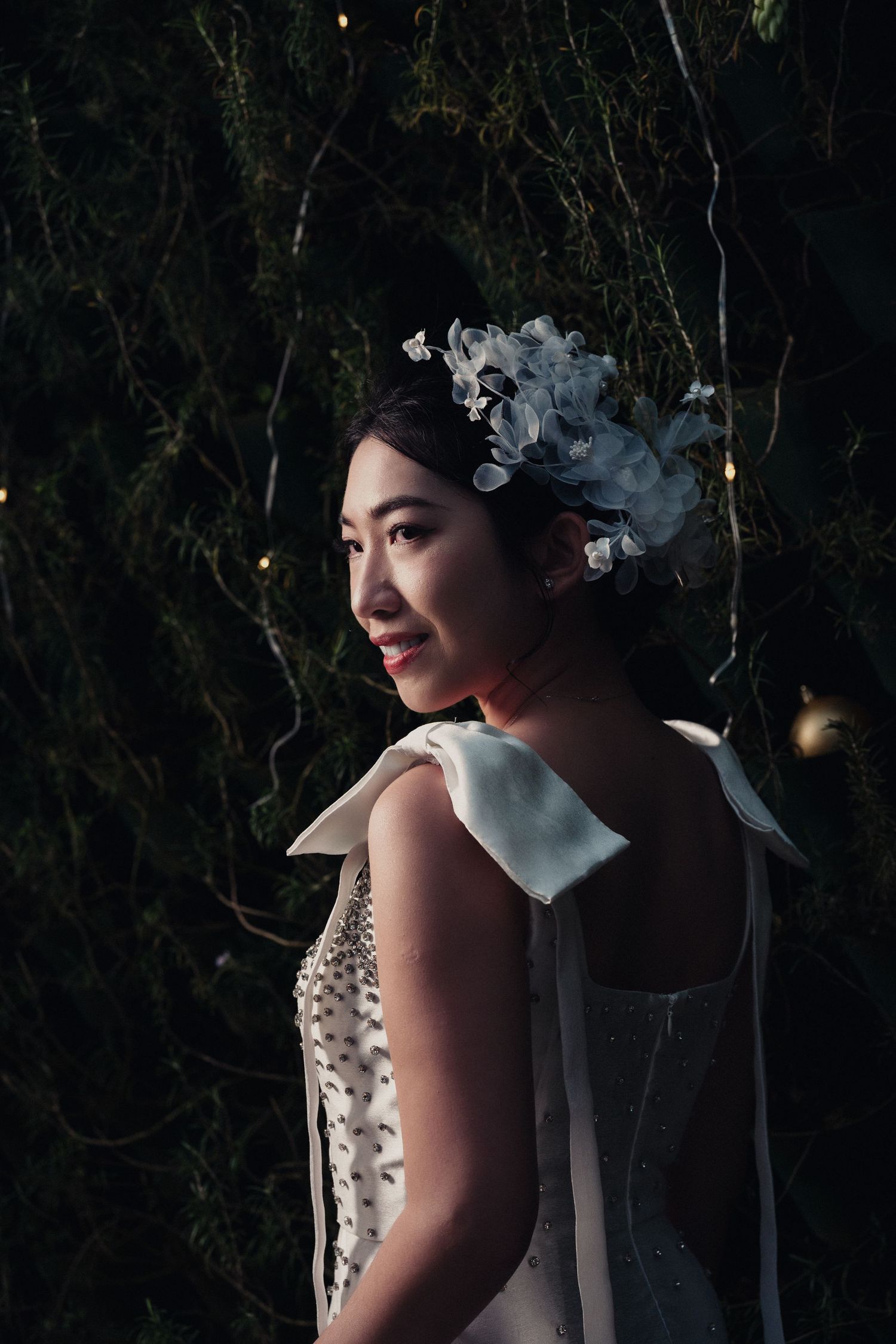 A bride in a white floral headpiece stands in dramatic lighting against a dark background.
