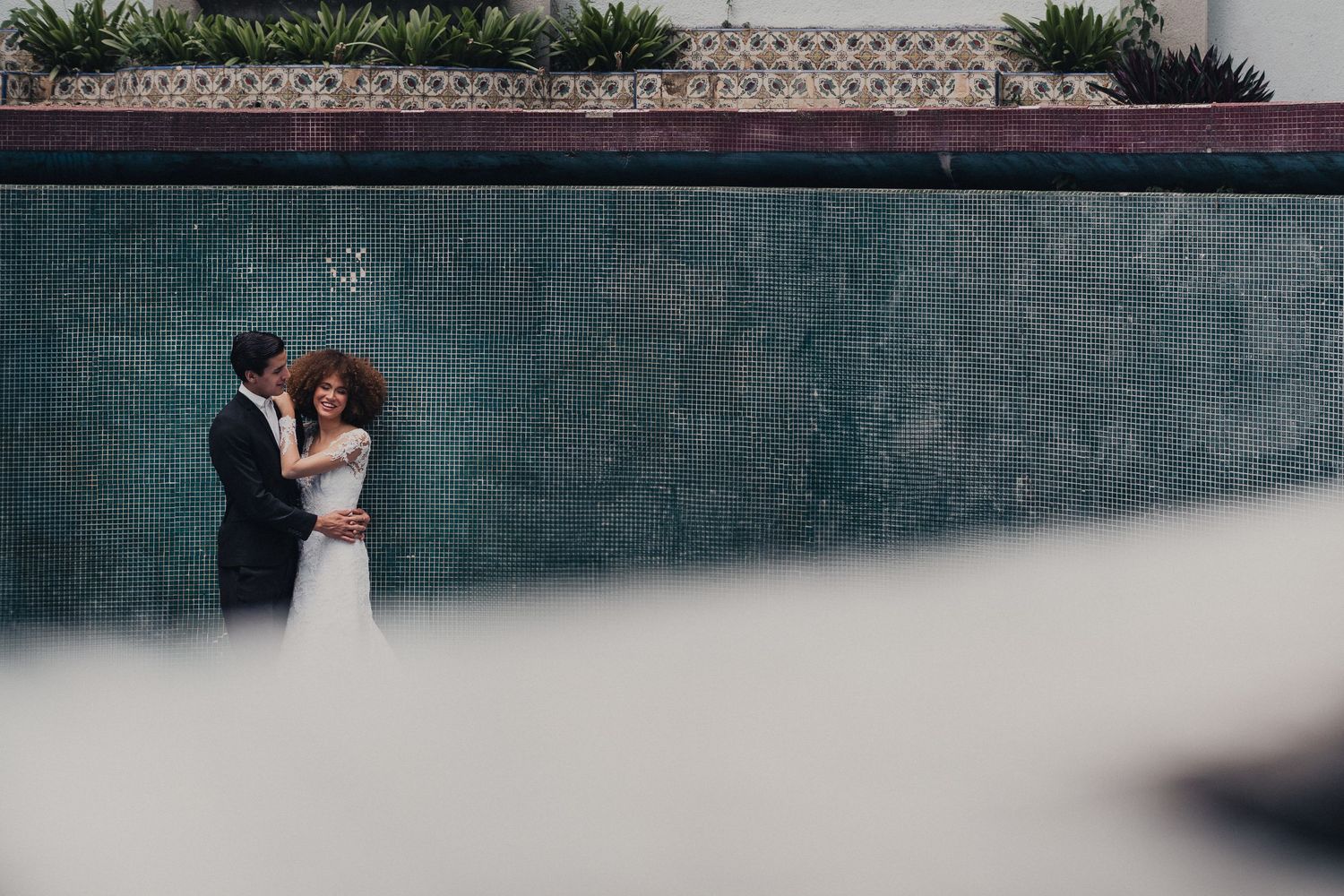 A couple embraces romantically against a textured stone wall with dramatic lighting and shadows.