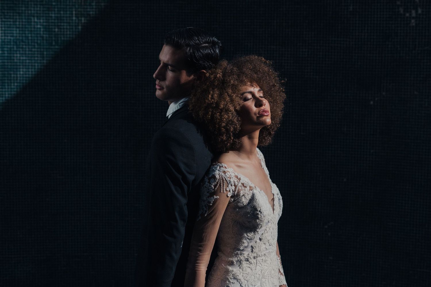 A couple in elegant wedding attire share an intimate dance together in a dimly lit setting.