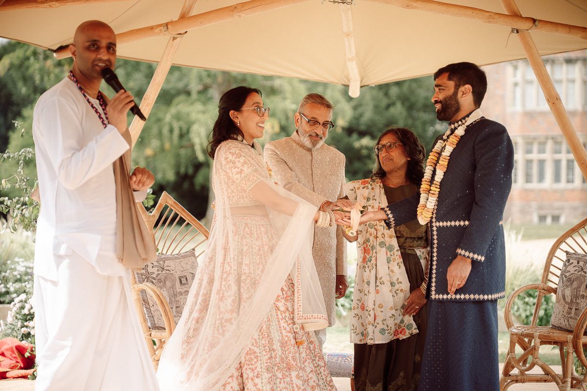 Wedding party members dance and celebrate under a white tent during an outdoor reception.