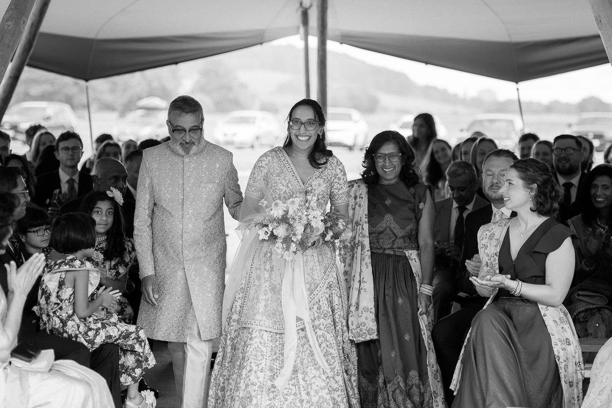Wedding guests stand in a receiving line under white tents during an outdoor celebration.