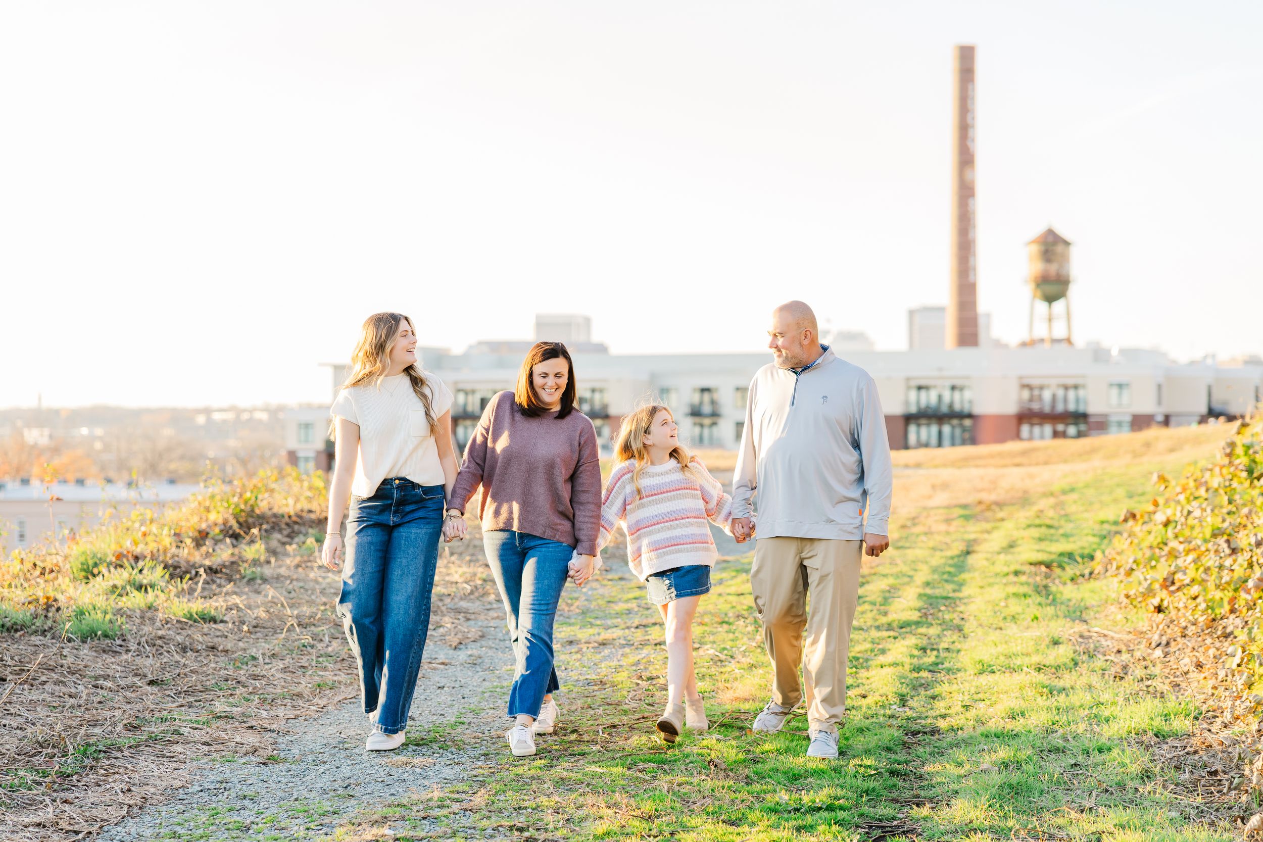 A family walks together on a grassy hill during golden hour with an industrial smokestack visible in the background at Libby Hill Park