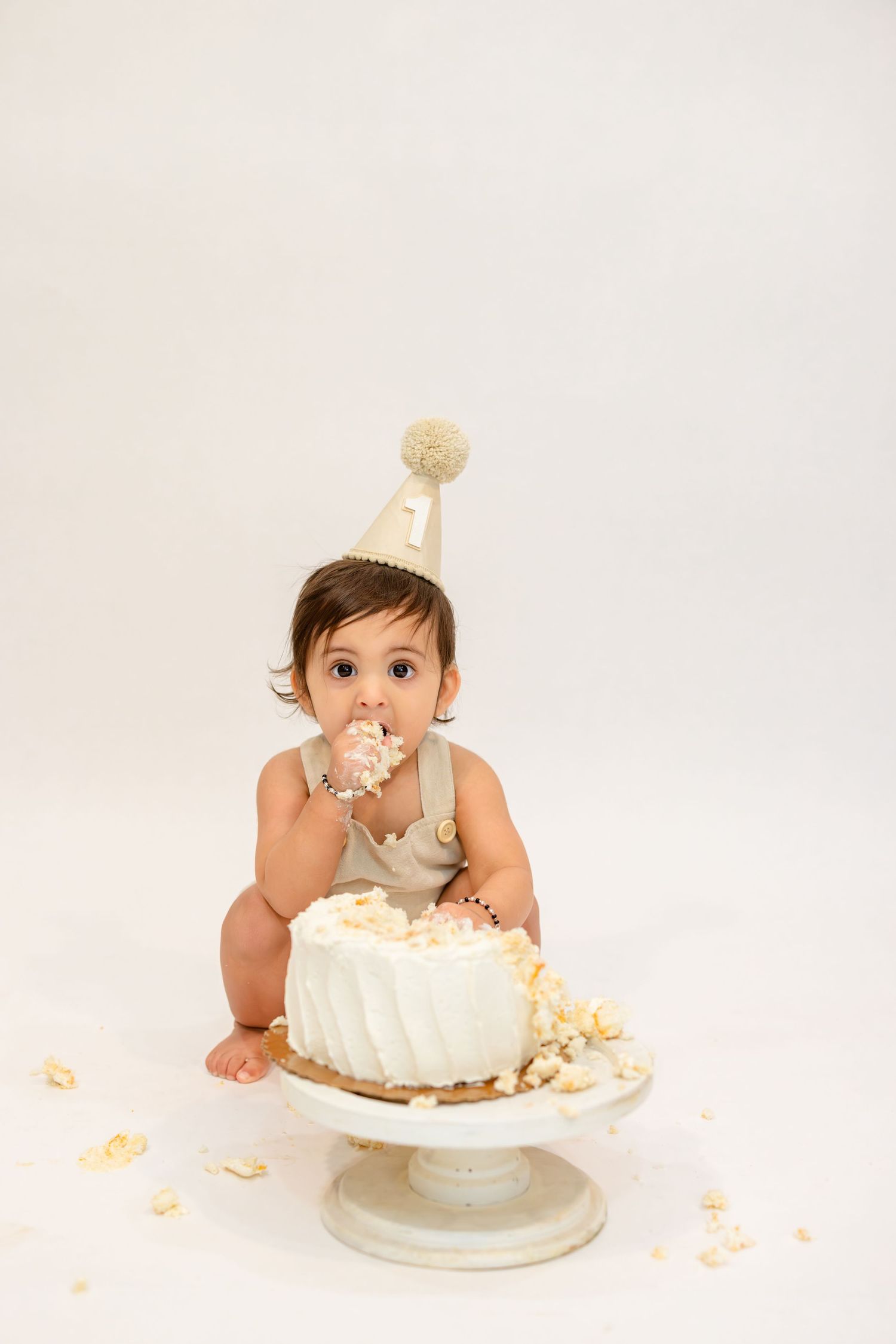 A baby wearing a party hat explores a white birthday cake in a series of progressive cake smash photos.