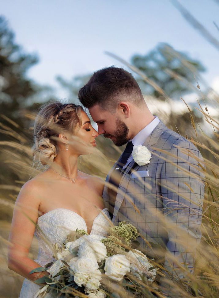 Bride and groom share an intimate moment surrounded by golden wild grass in a dreamy outdoor setting.