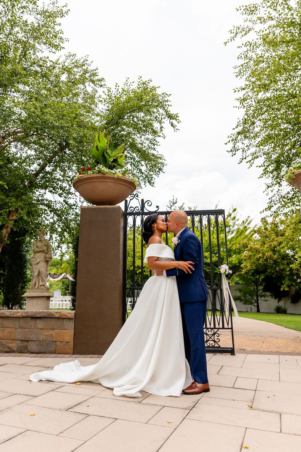 Wedding couple embracing on a stone terrace with decorative iron gates and garden views at Villa Aletta in Omaha, NE.