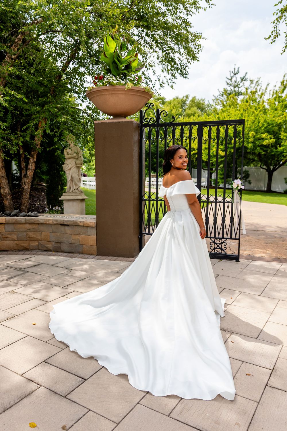 Stunning white wedding gown with dramatic train flowing across stone patio in outdoor garden setting.