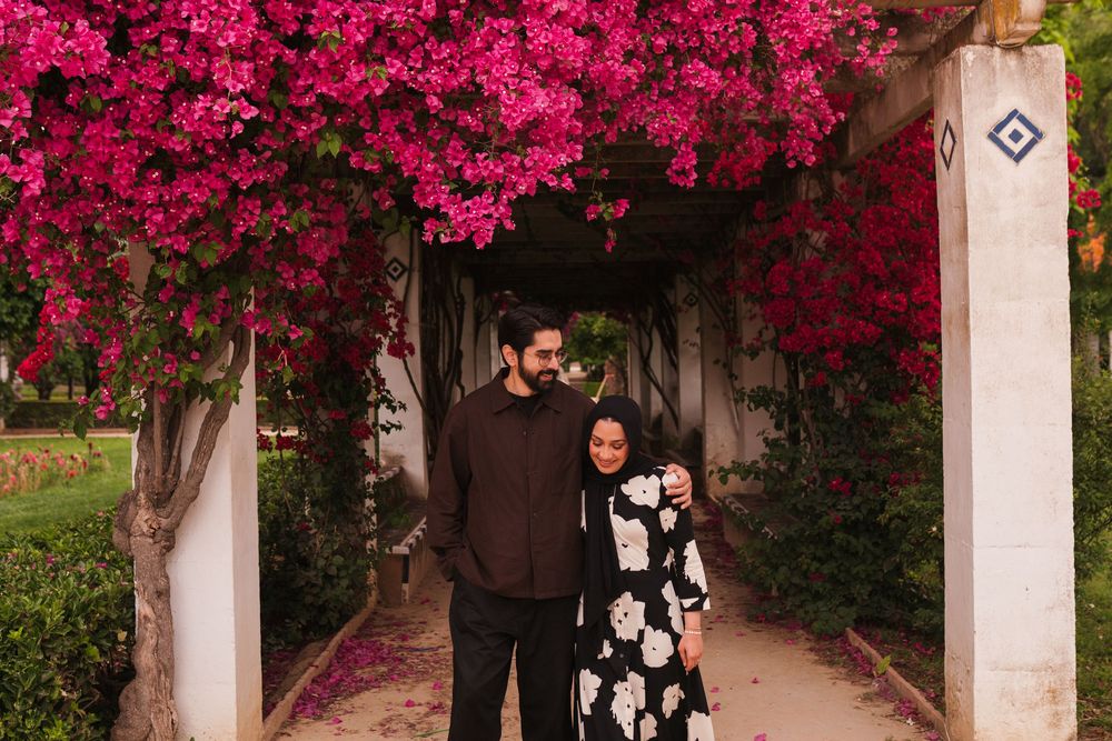 Couple embracing under vibrant pink bougainvillea archway in a lush garden pathway.