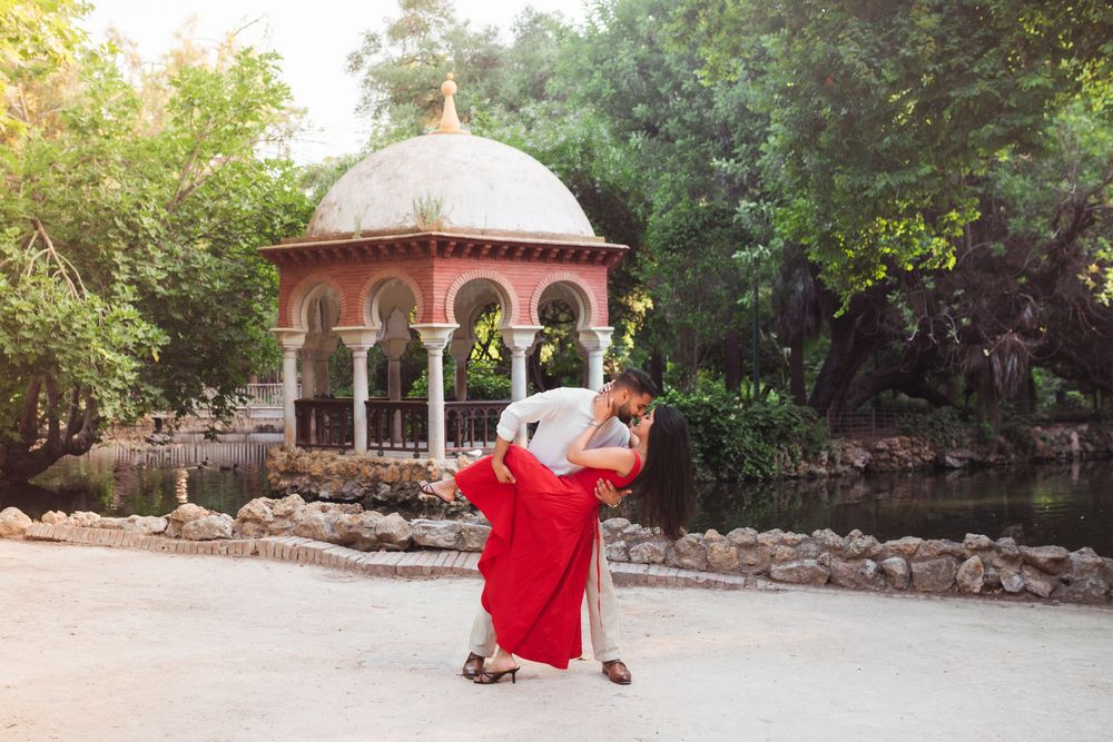 A romantic moment captured in front of an ornate stone gazebo with a domed roof in a garden setting.