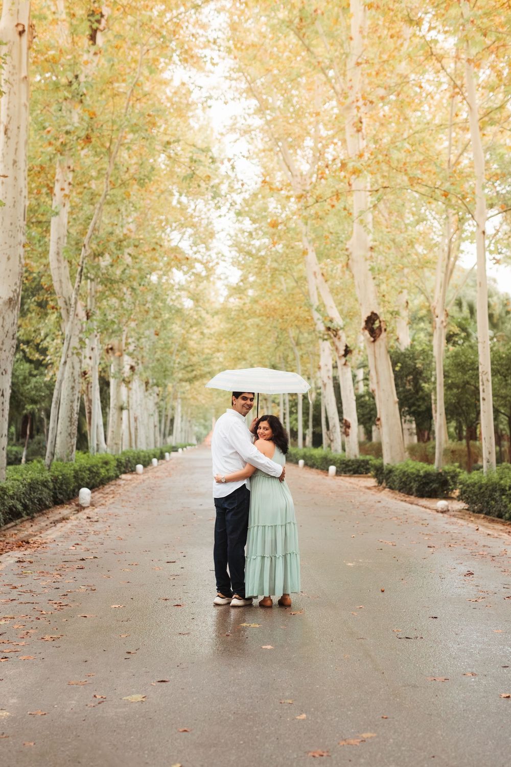 A couple strolls together down a tree-lined path during autumn with golden leaves overhead.