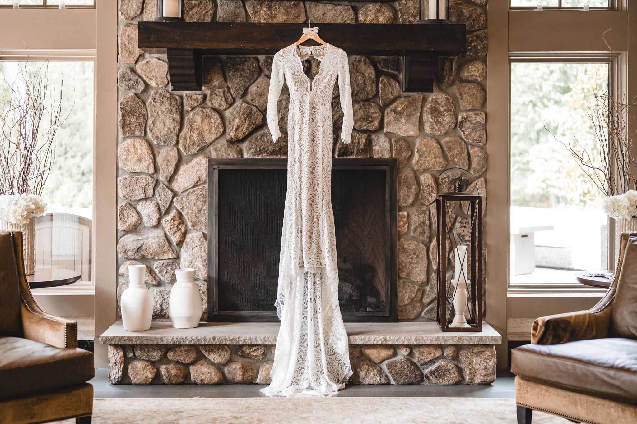 Wedding dress hanging in rustic stone fireplace room with natural window light.