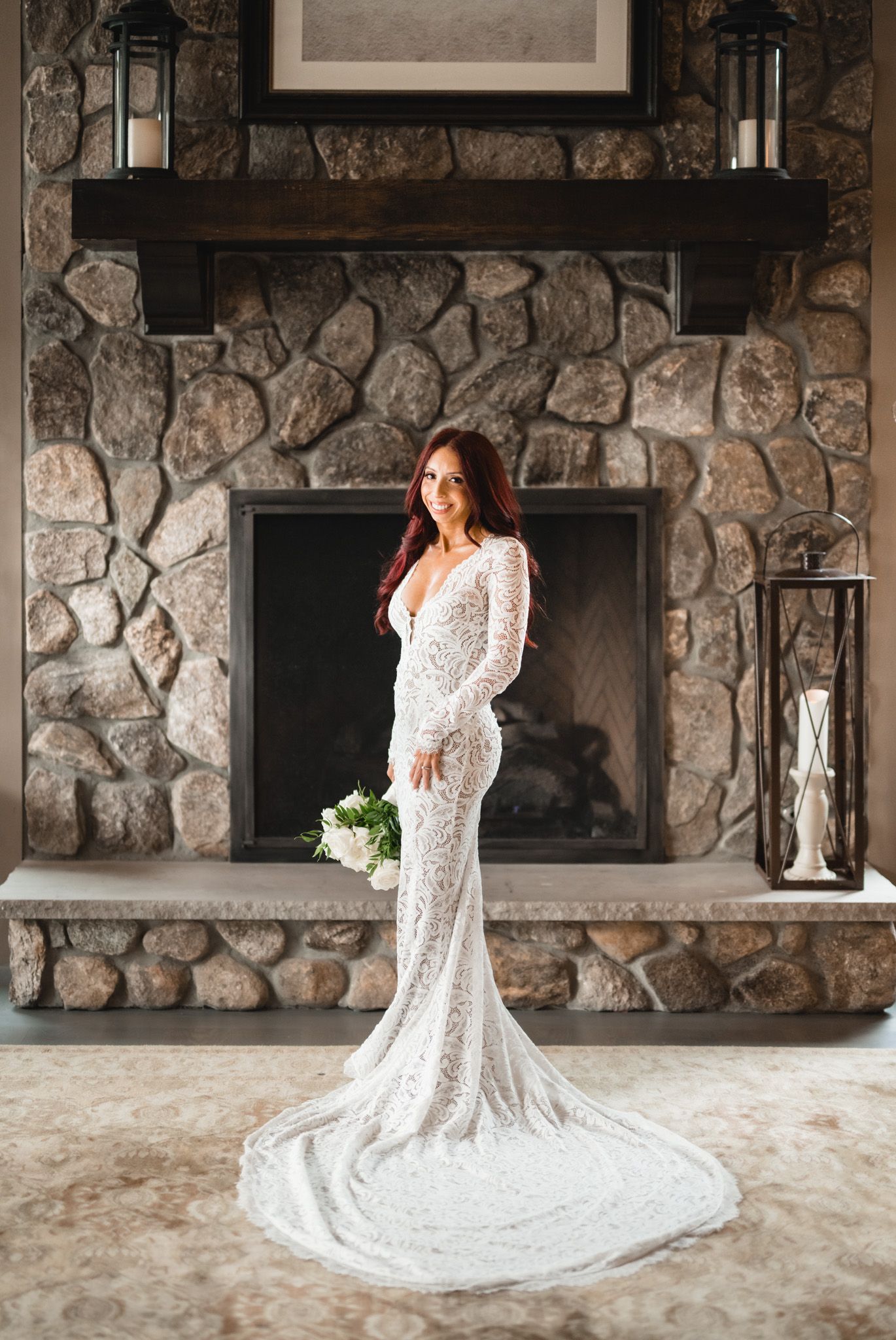 A stunning lace wedding gown with long train photographed against a stone wall backdrop.