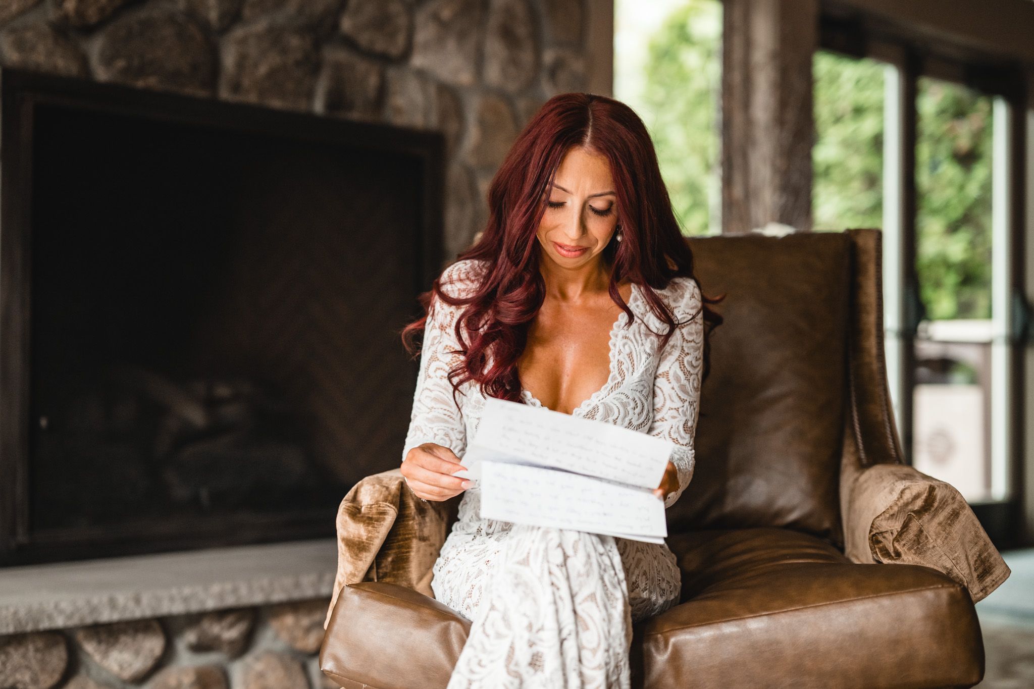 Bride in lace gown reading a letter in a rustic room with leather furniture.