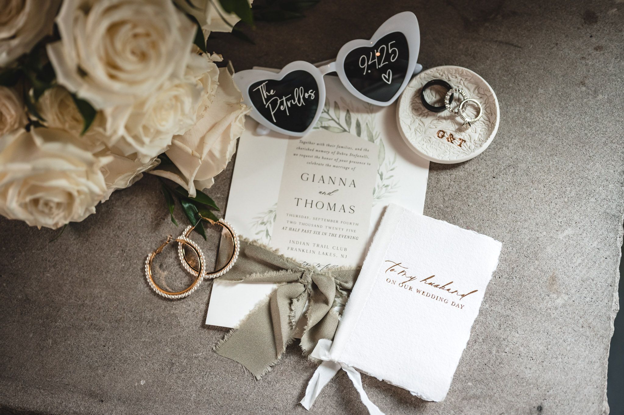 Wedding details including white roses, rings, and black chalkboard signs on gray surface.