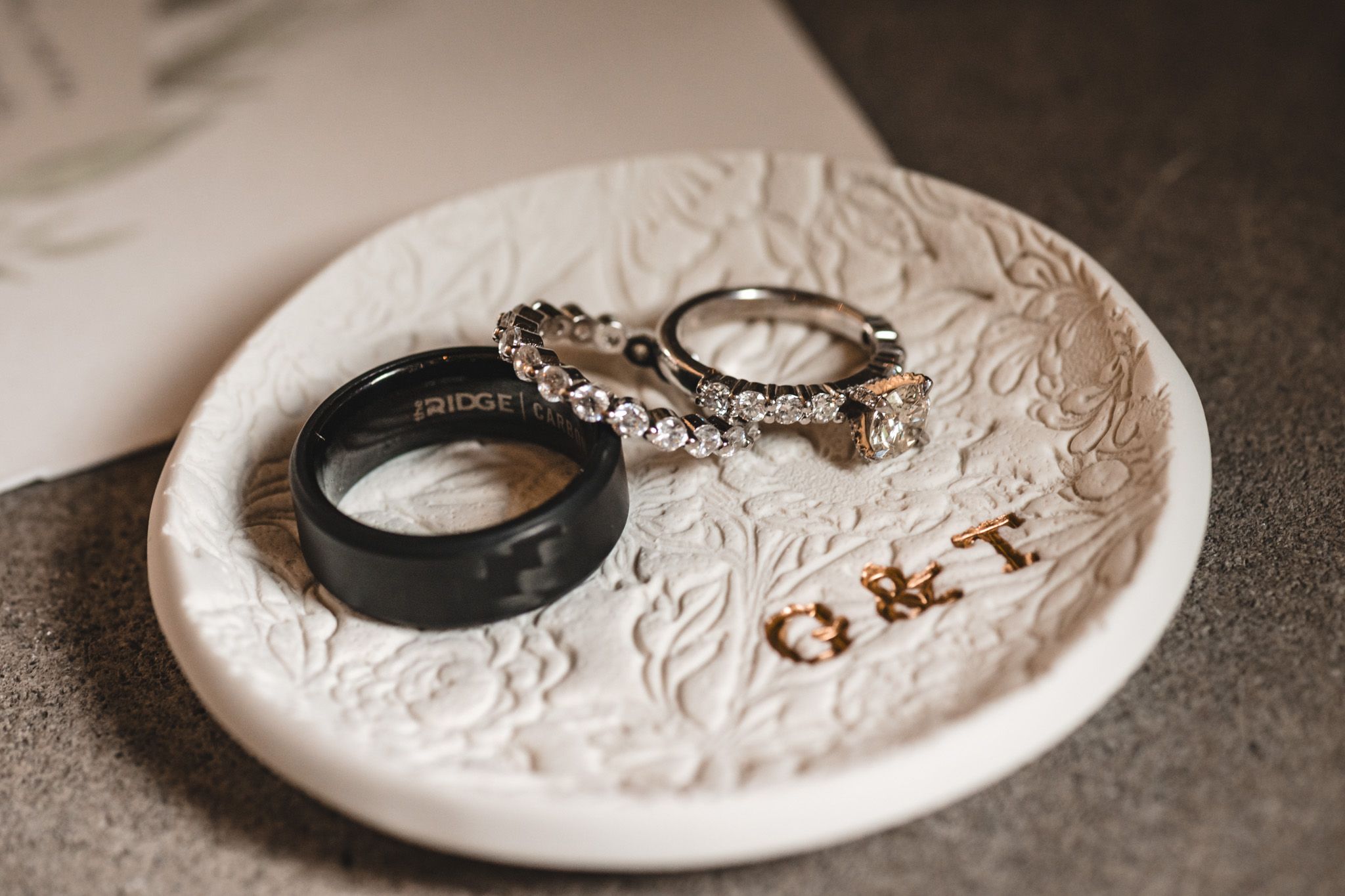 Wedding rings and decorative details arranged on textured white ceramic plate.