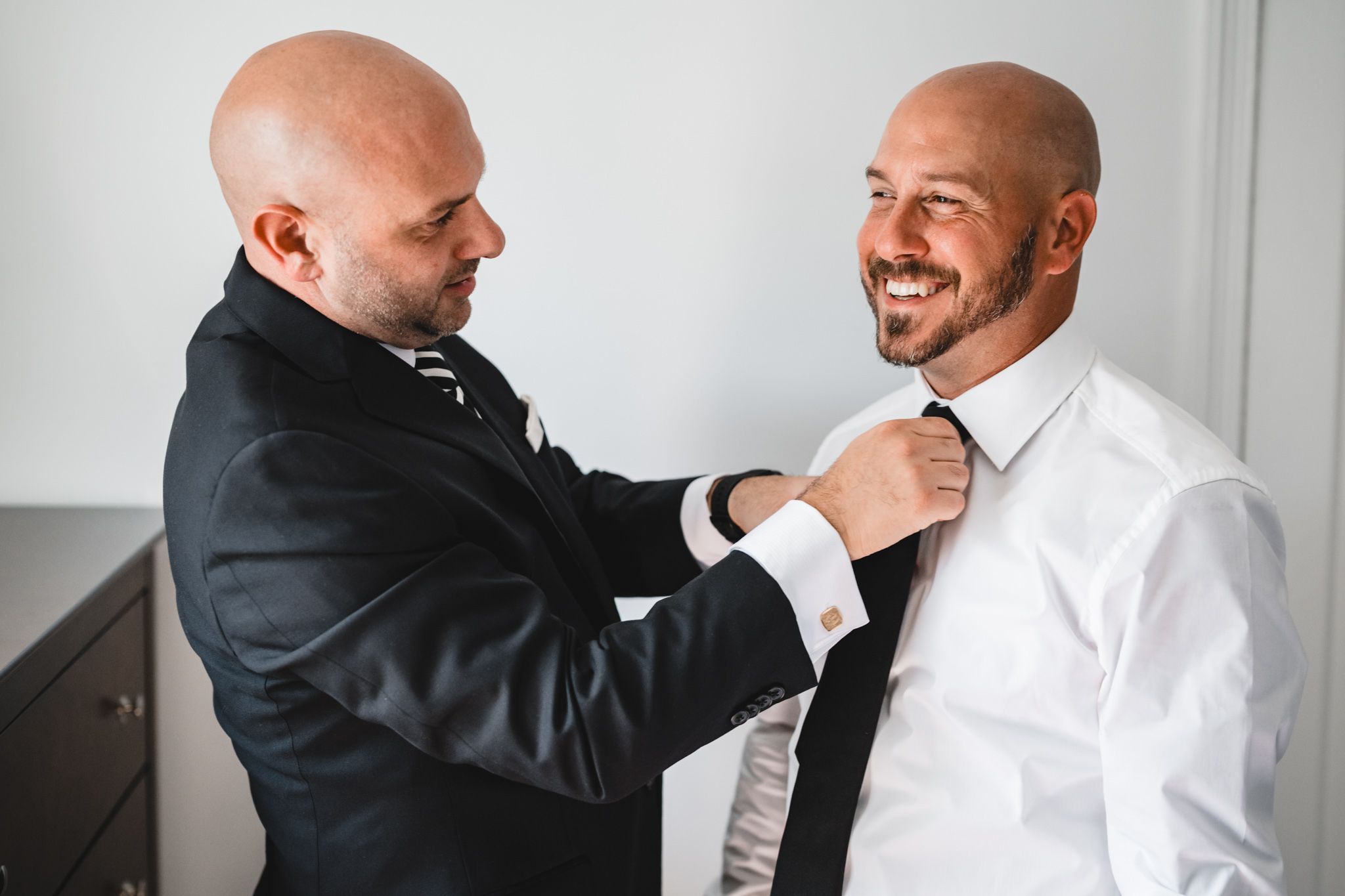Men in formal attire helping each other get dressed for a special occasion.