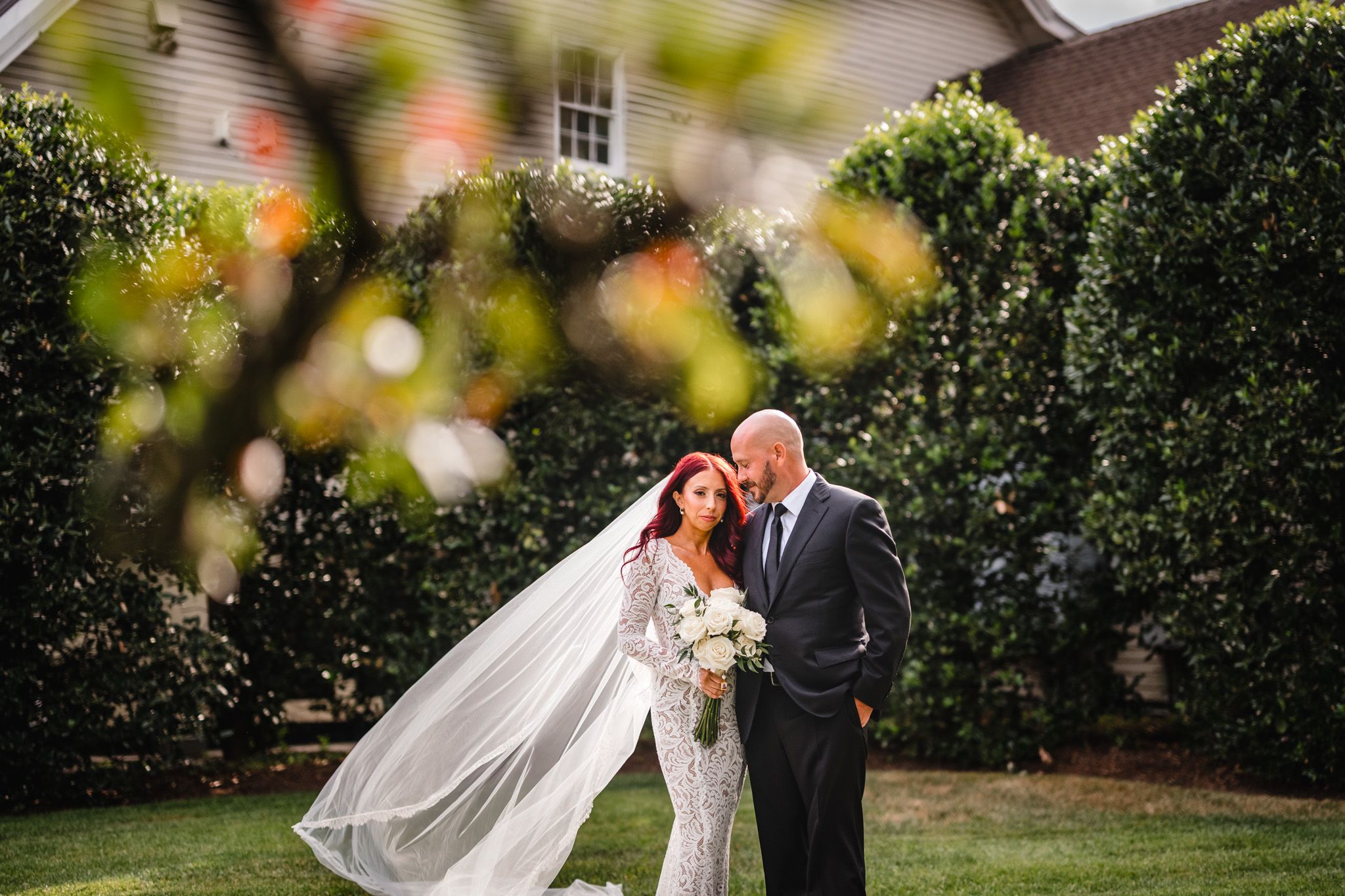 An intimate garden wedding moment with flowing veil against greenery backdrop.