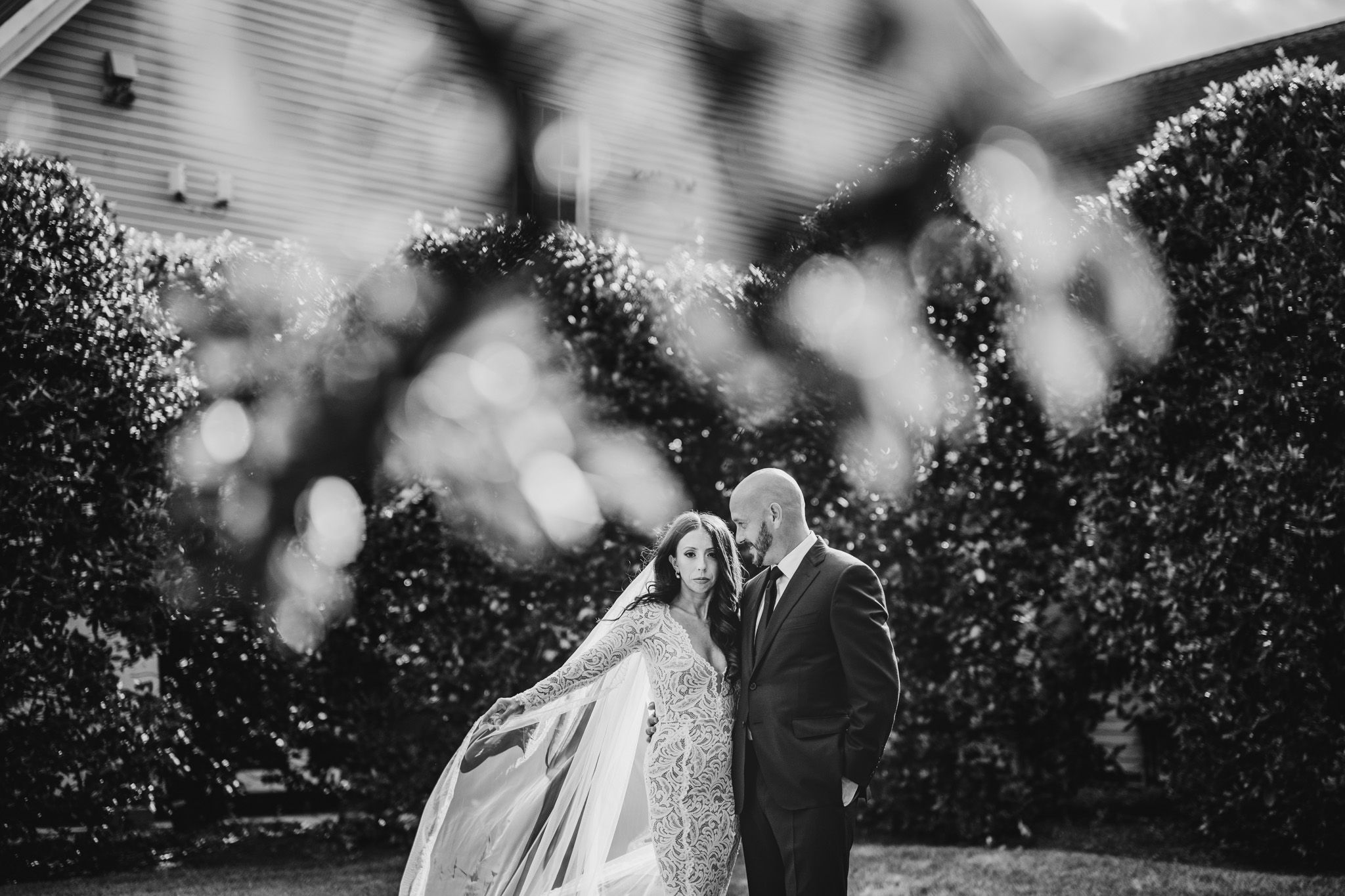 A black and white wedding portrait with artistic bokeh effect in garden setting.
