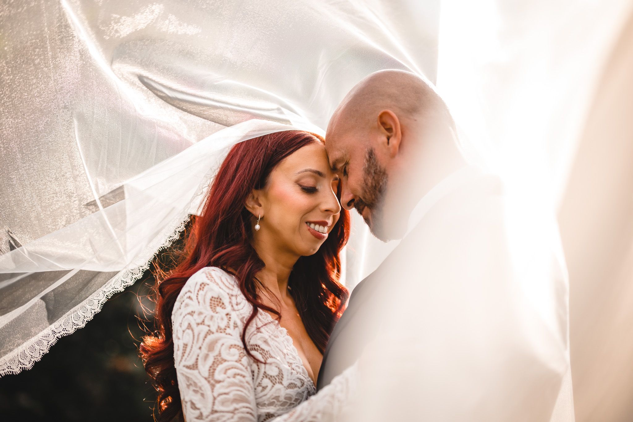 Intimate wedding moment captured under flowing white veil.