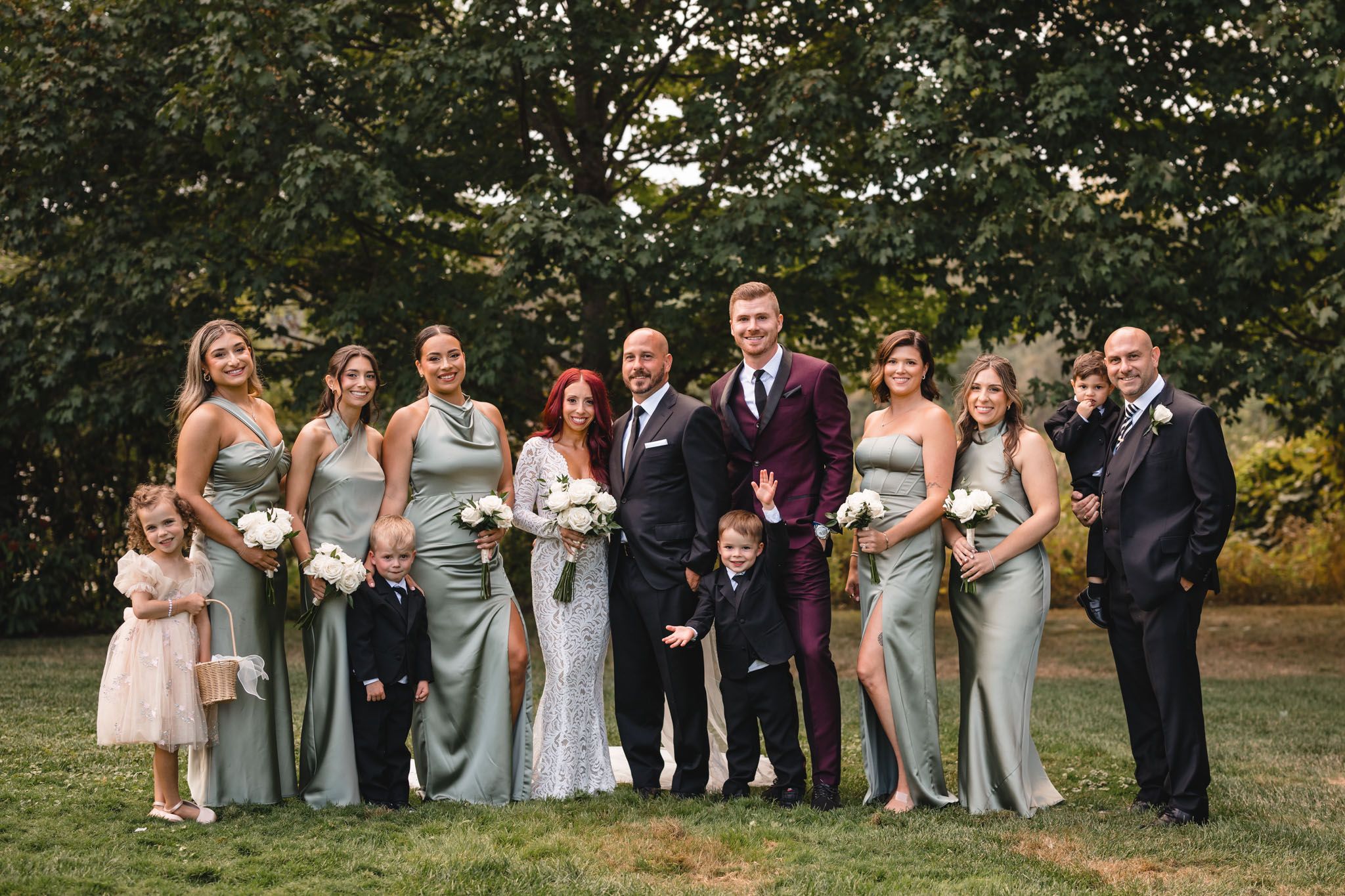 Wedding party group photo with bridesmaids in pastel dresses on a sunny lawn.