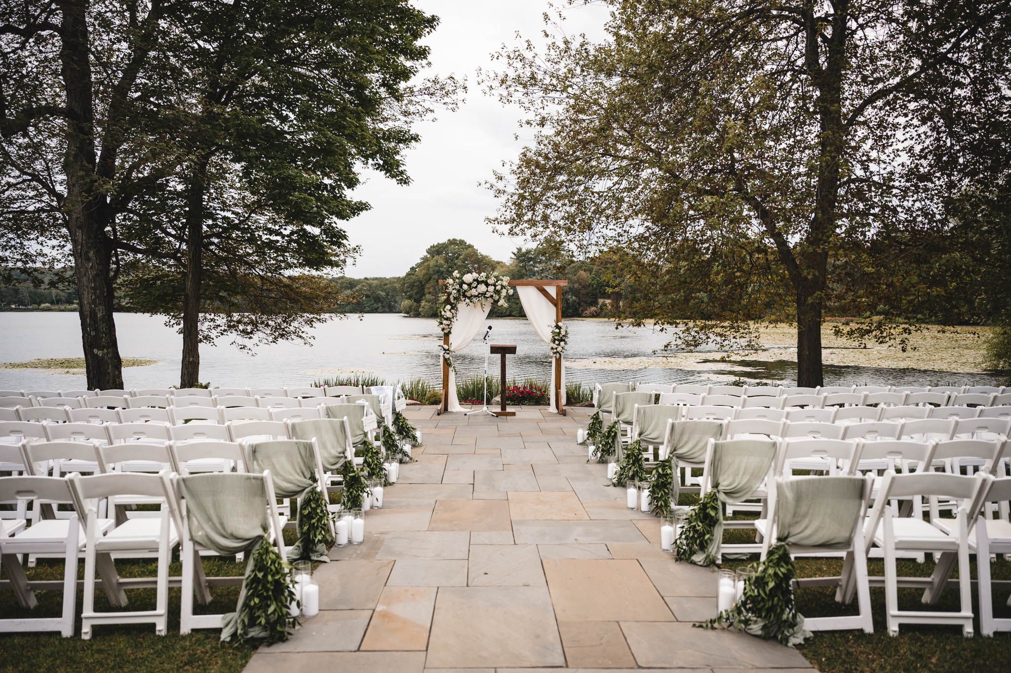 Outdoor wedding ceremony setup with white chairs arranged on a stone patio.