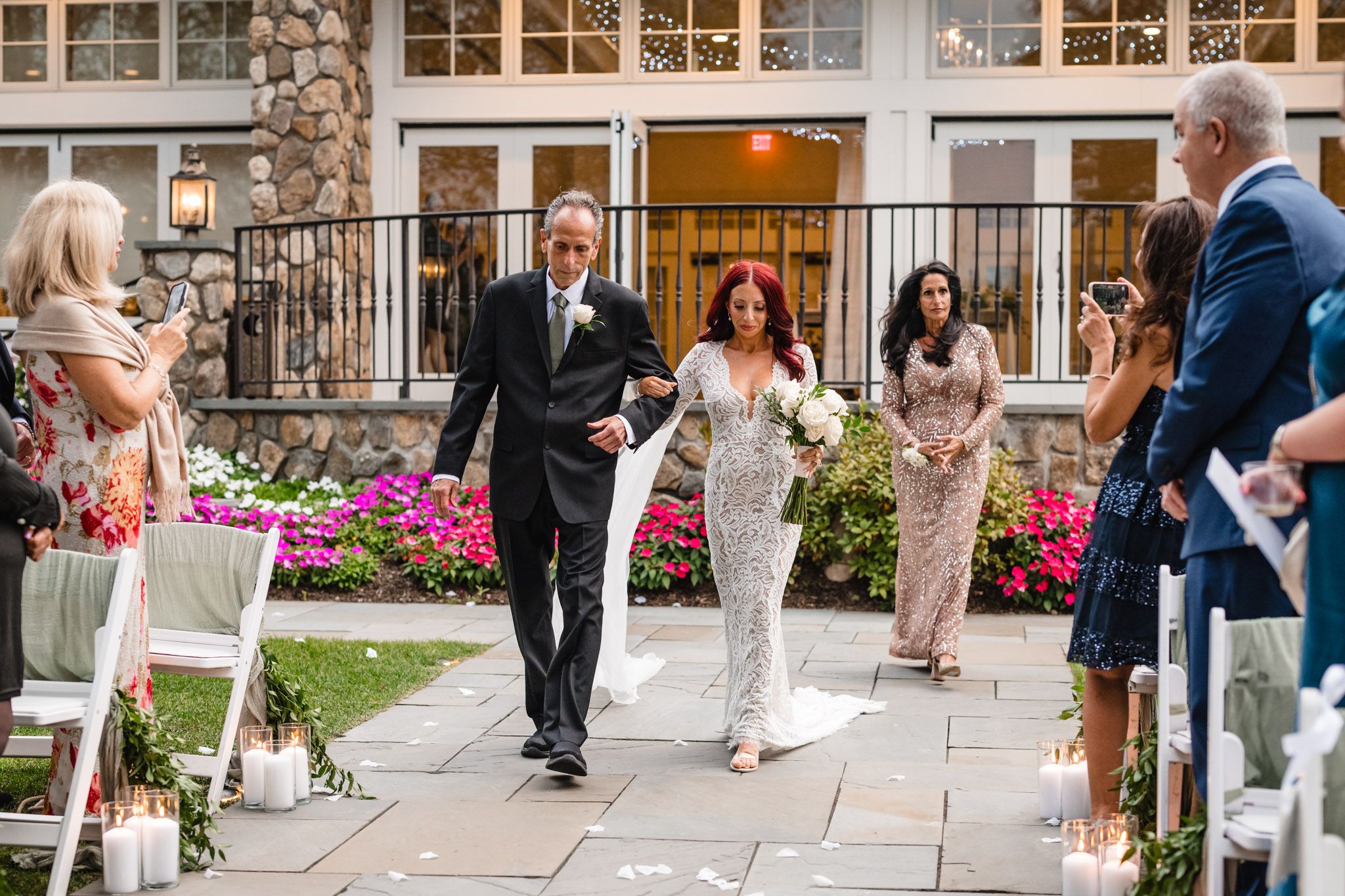 Wedding ceremony processional with couple walking down aisle decorated with pink flowers and white decor.