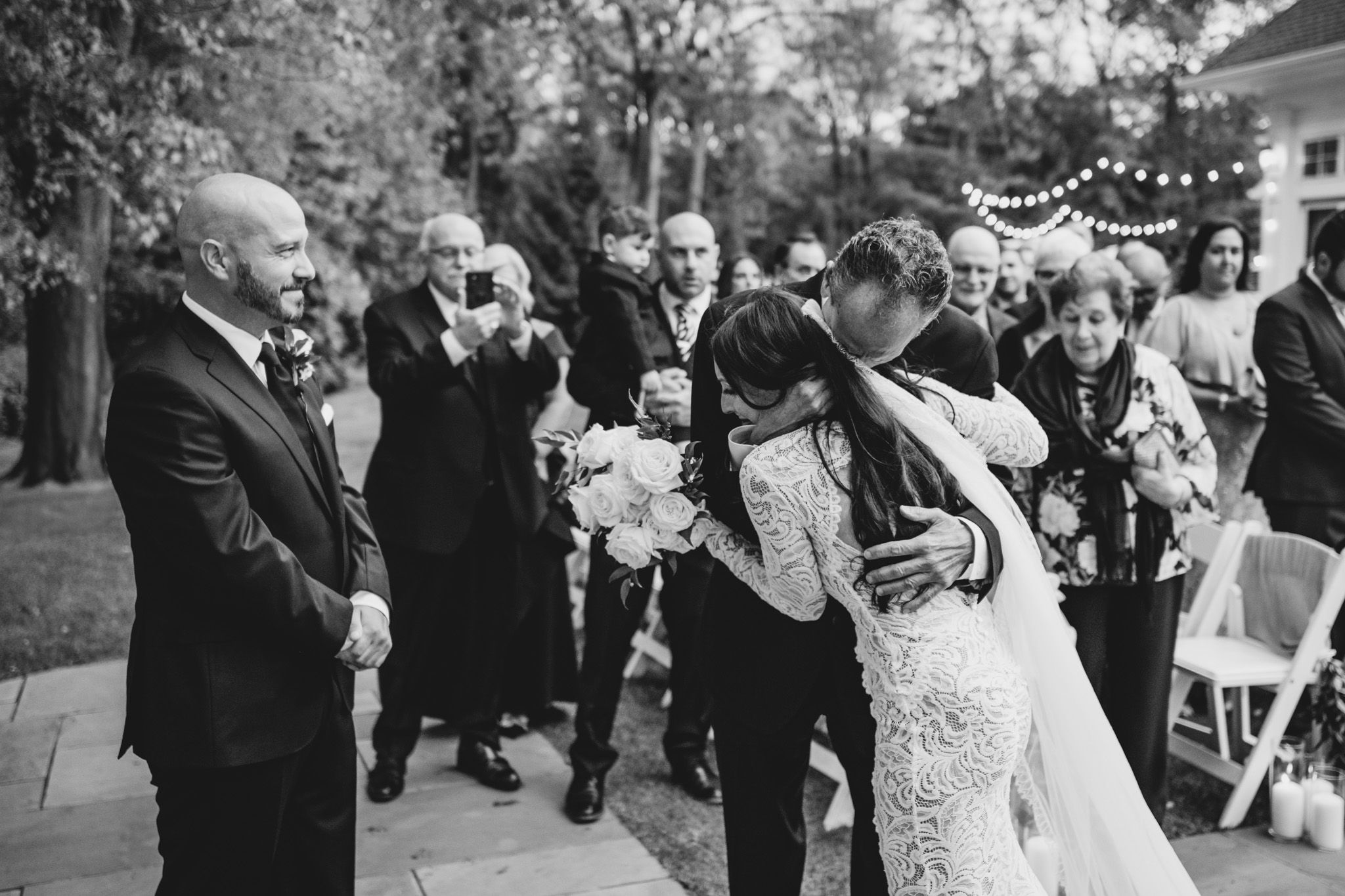 Black and white photo of wedding celebration with guests gathered outdoors.