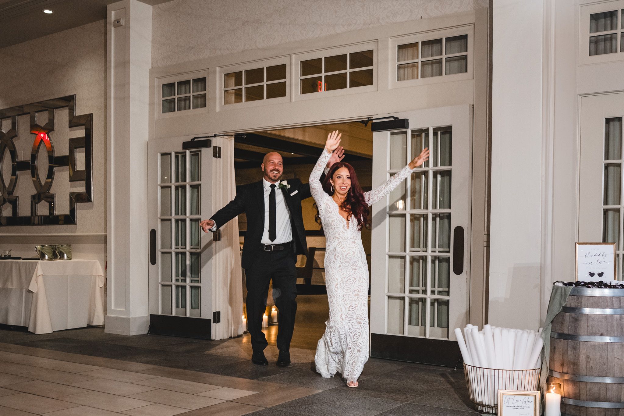 Joyful entrance into wedding reception venue with French doors and white decor.