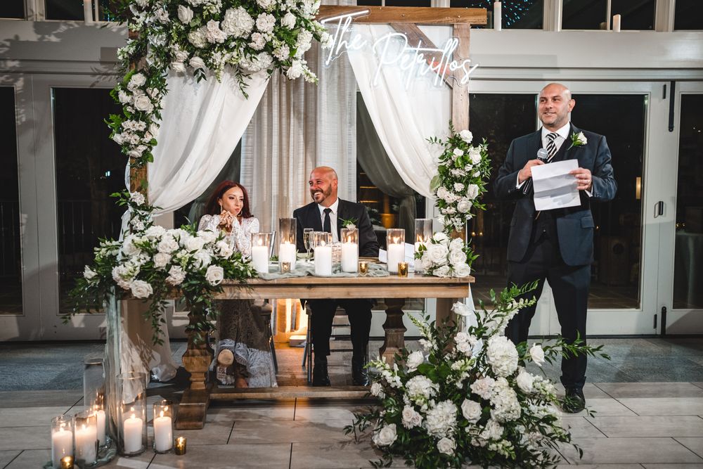 Wedding reception setup with elegant white floral arrangements and candles at the head table.