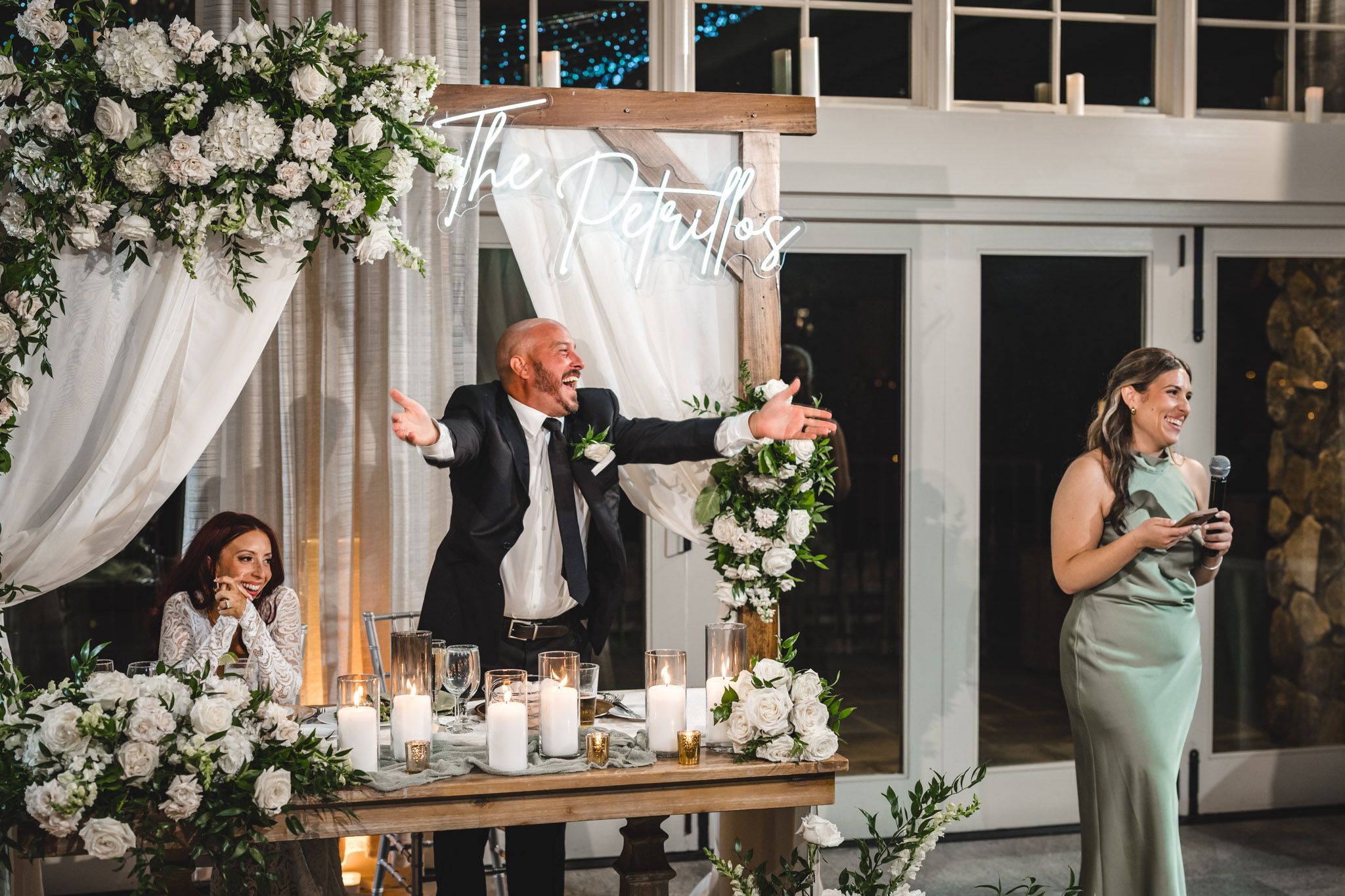 Wedding reception head table with elegant white floral arrangements and draped fabric decor.