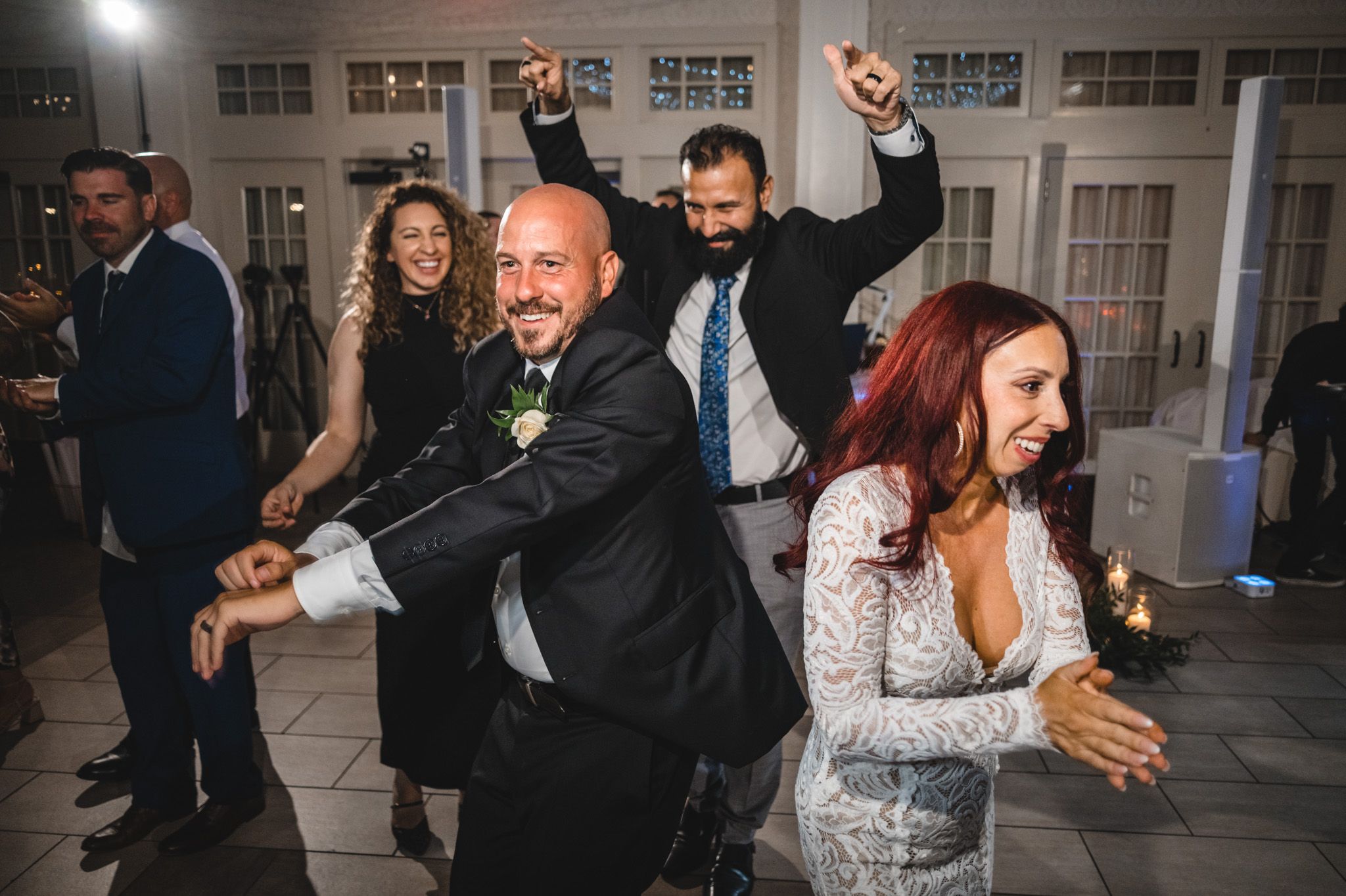 Wedding party dancing and celebrating during reception in a brightly lit venue.