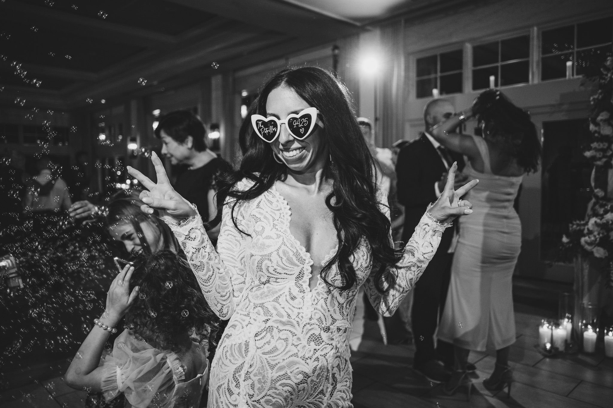 Wedding guests dancing and celebrating under decorative indoor lighting.