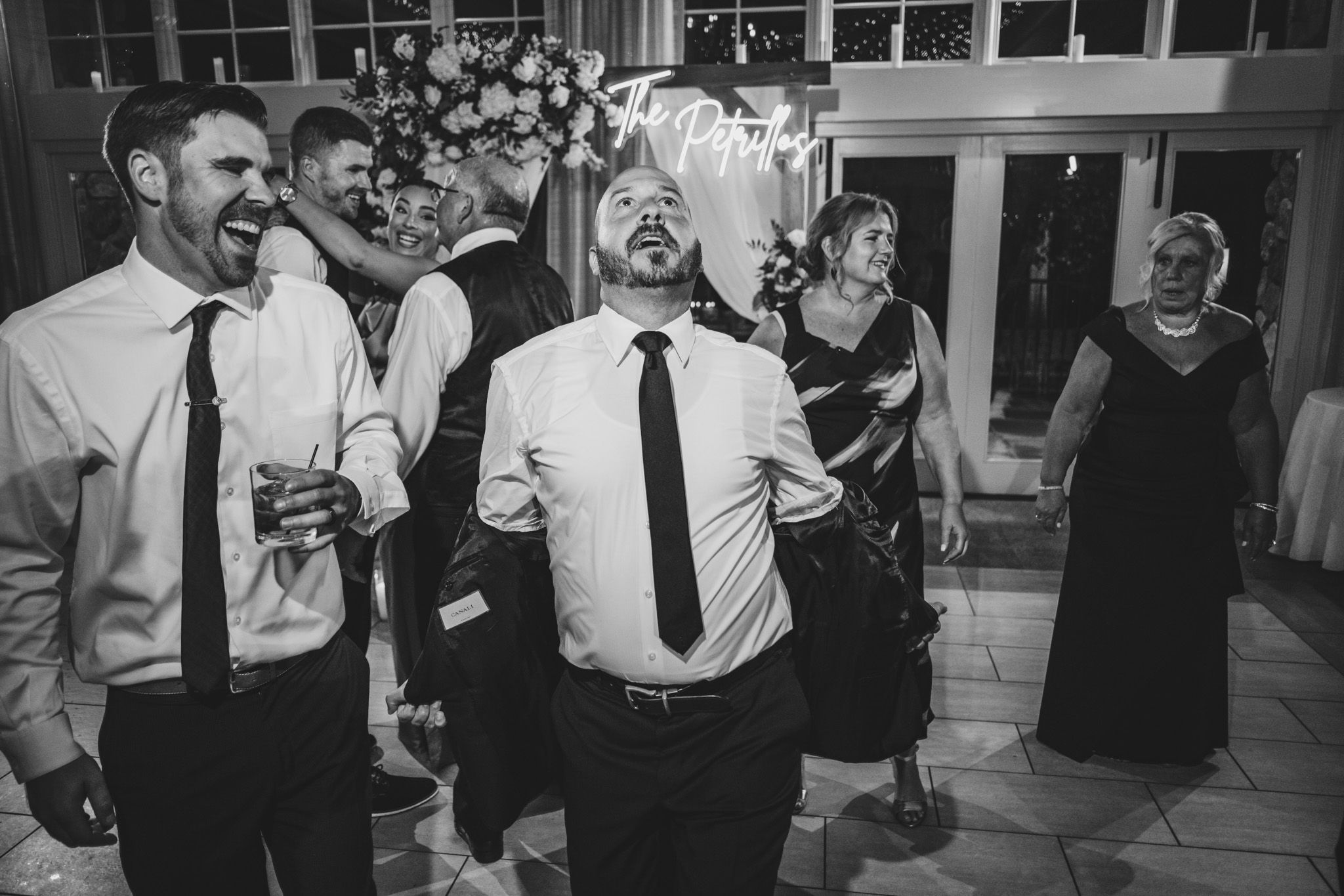 Black and white photo of wedding guests enjoying drinks and conversation at reception.