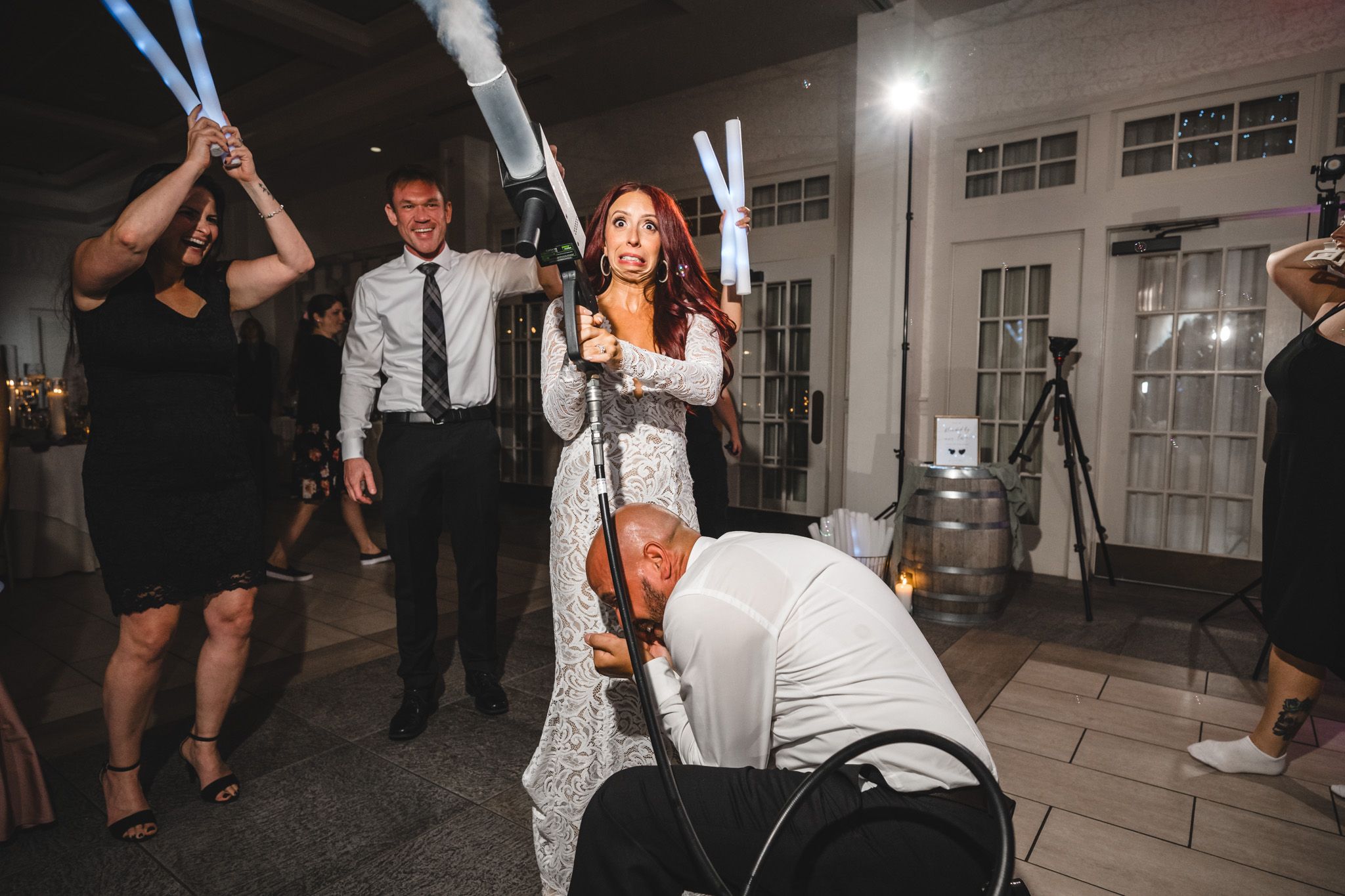 Wedding guests wave light sabers during an energetic dance party celebration with fog effects and string lights overhead.