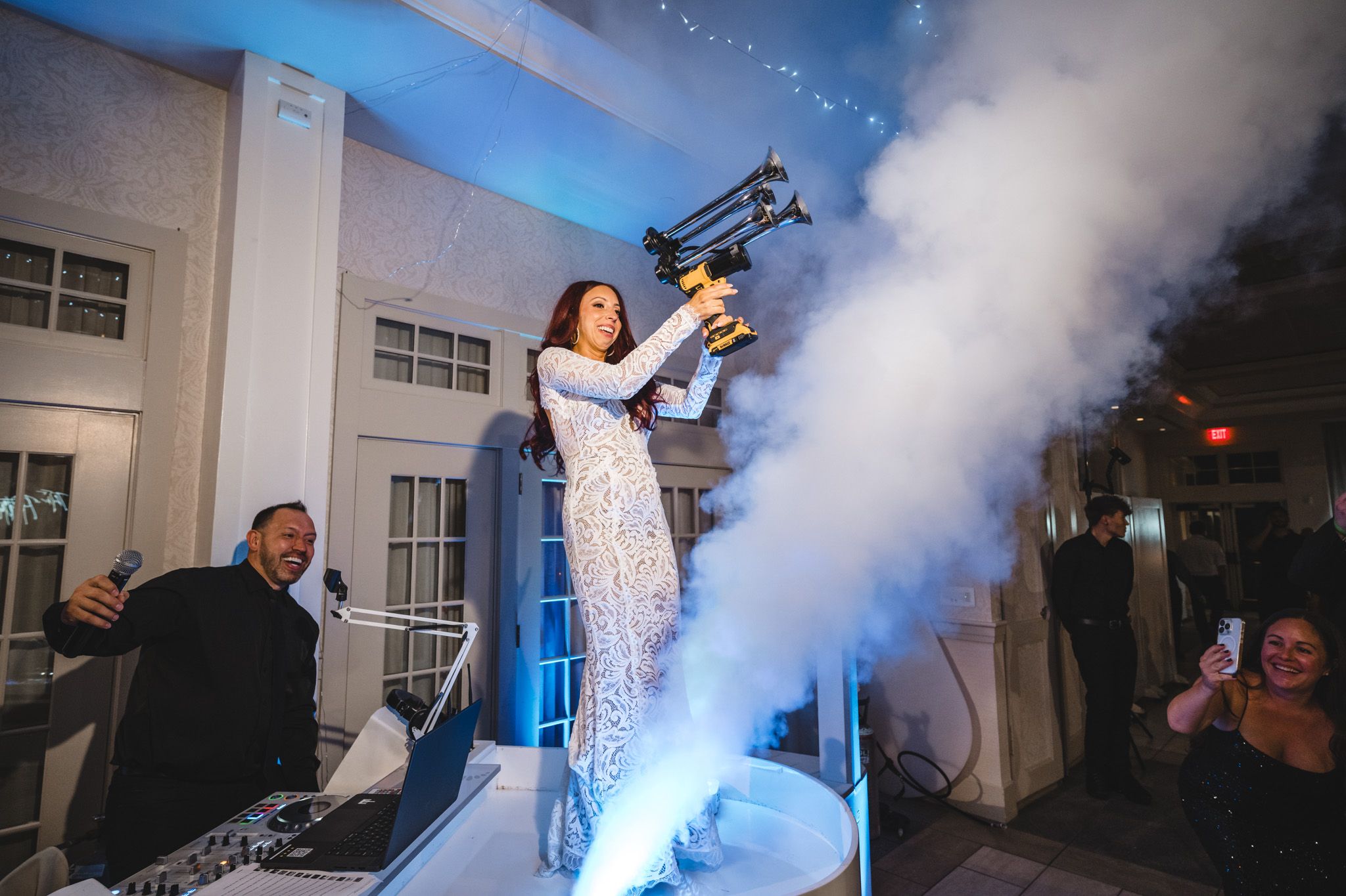 Blue fog effects and string lights create an atmospheric dance floor scene at a wedding reception.