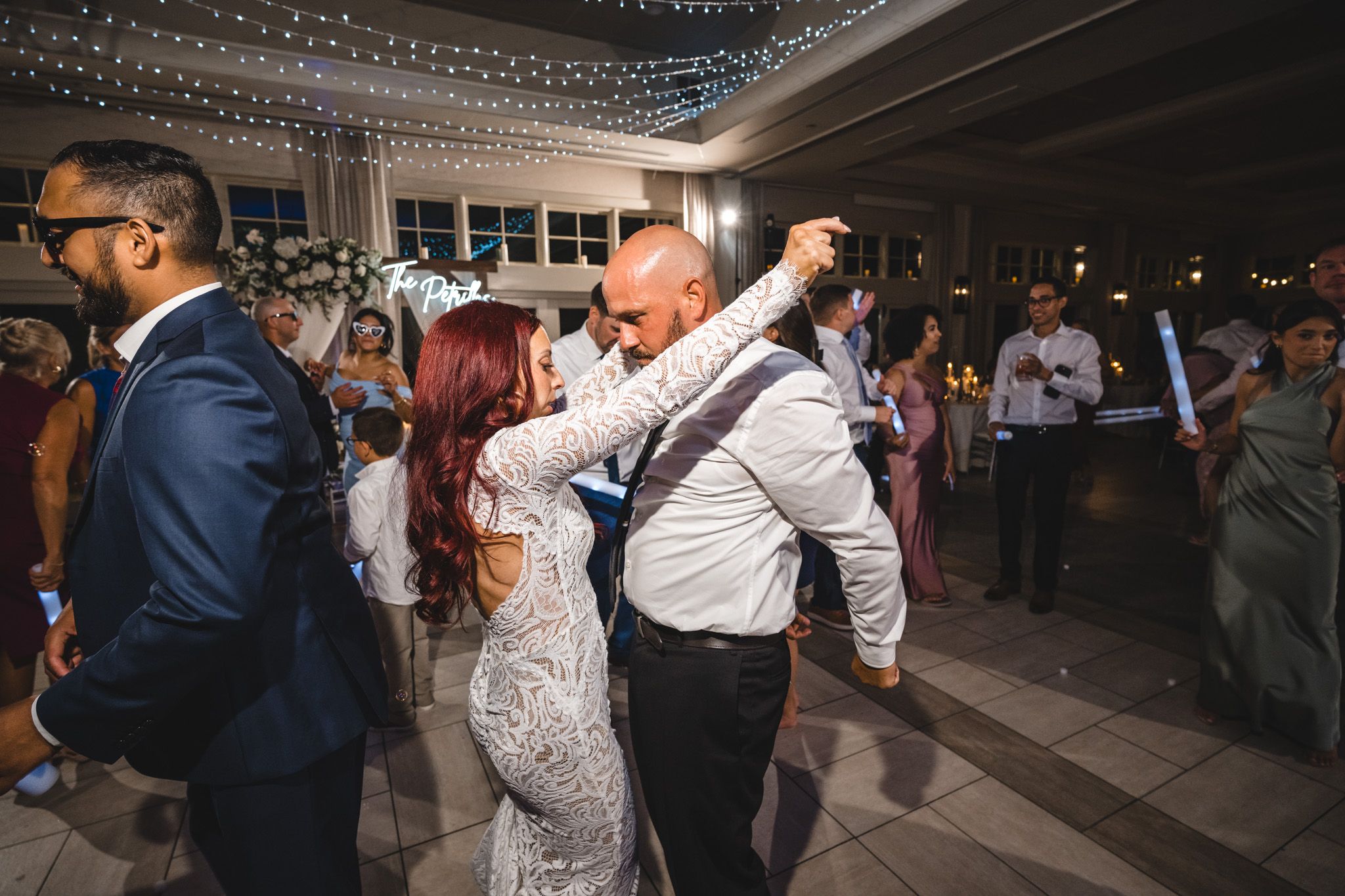 Wedding reception dance floor filled with guests waving LED light sabers under decorative string lighting.
